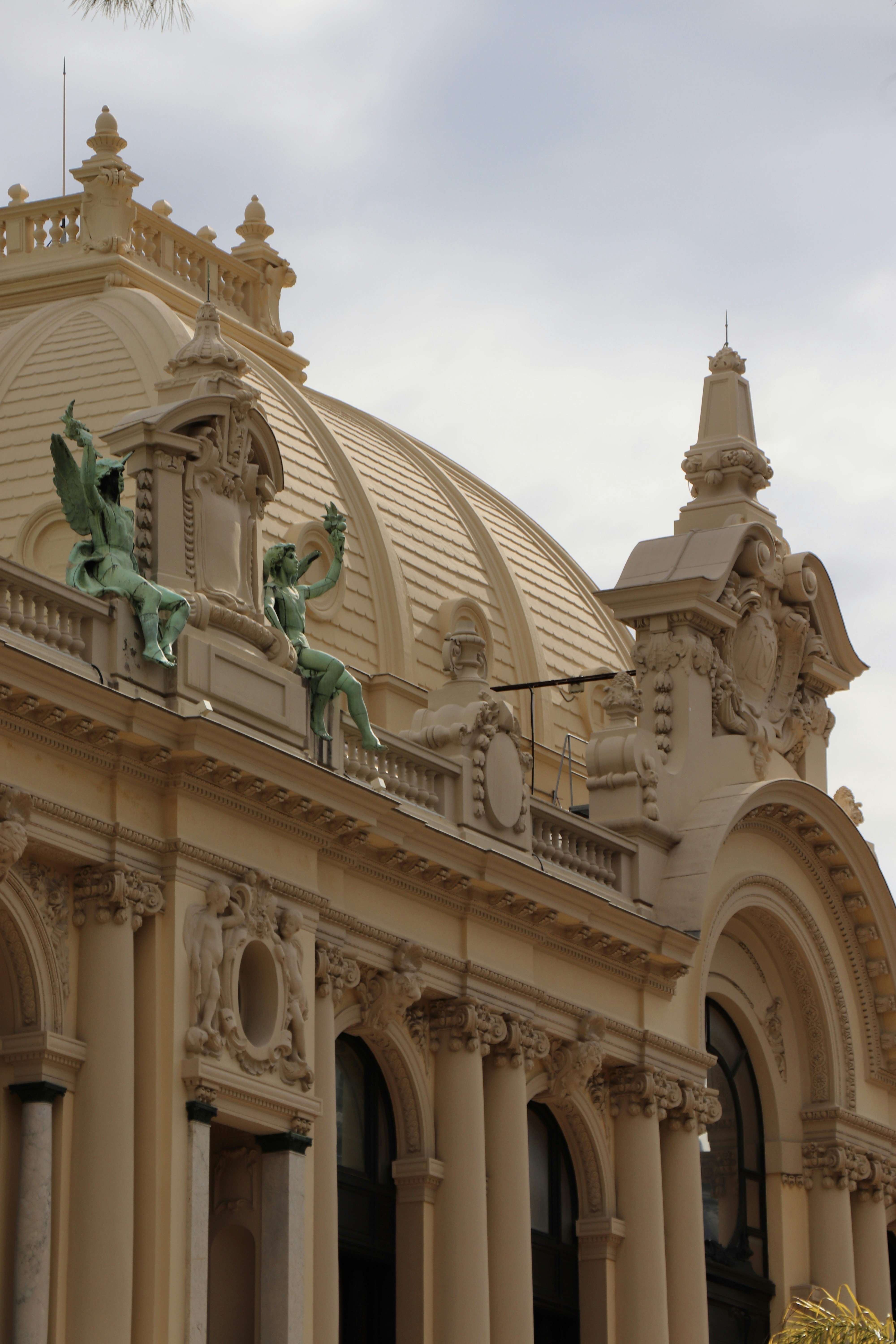 Two green statues of winged figures sitting on the ornate roof of the Monte Carlo Casino