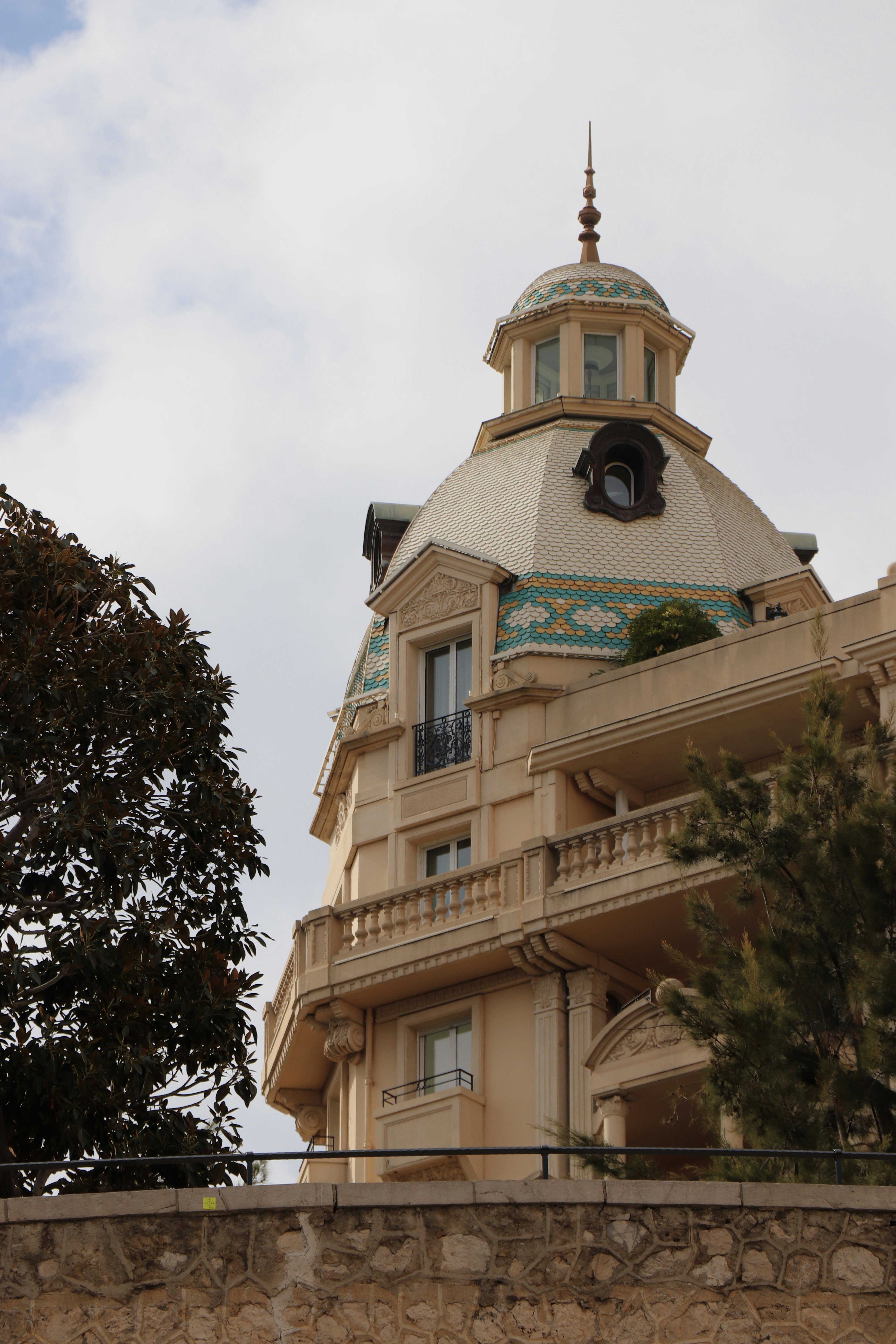 A beige building with a decorative tiled dome and balconies under a cloudy sky