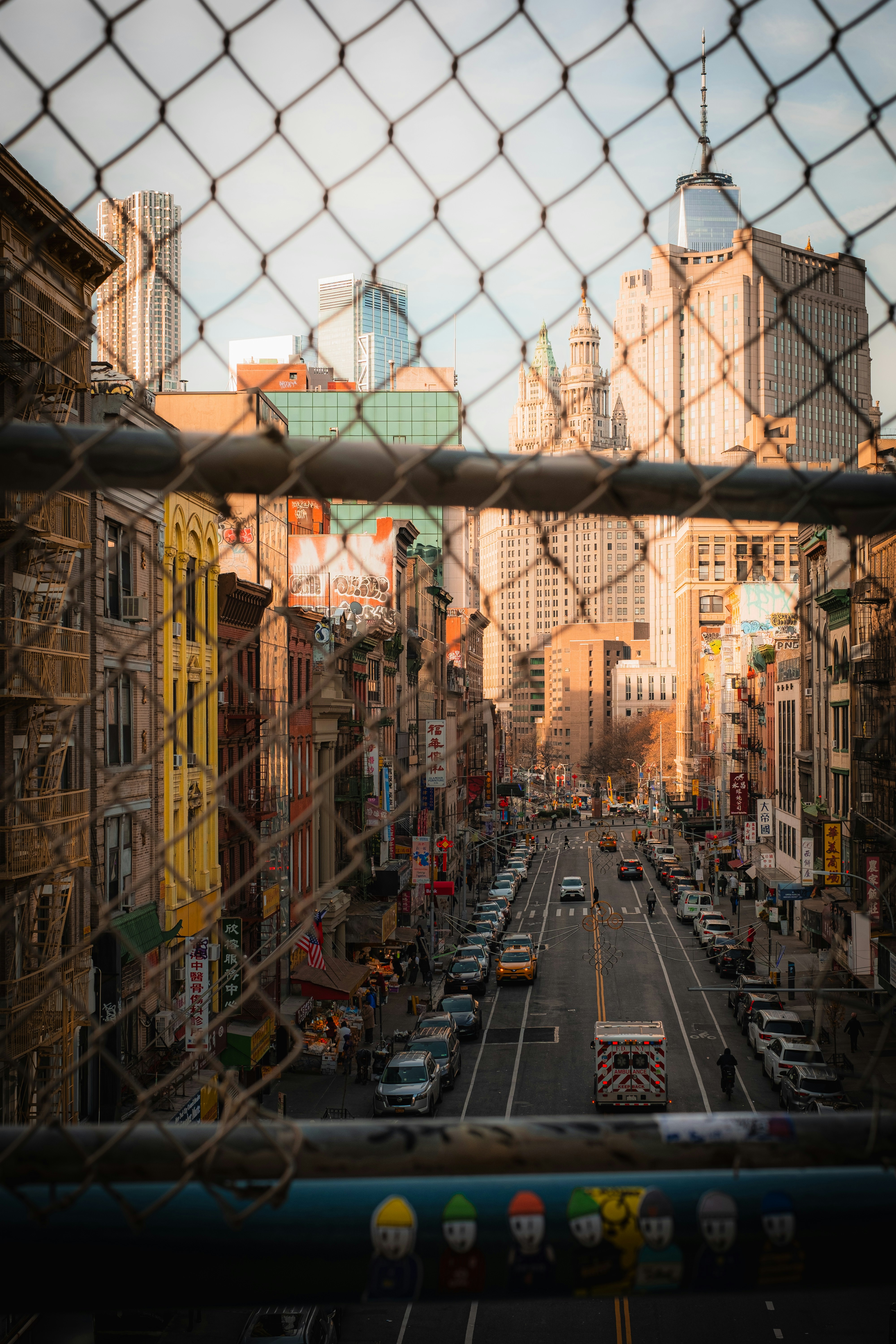 A city street in New York viewed through a chain link fence with tall buildings in the distance