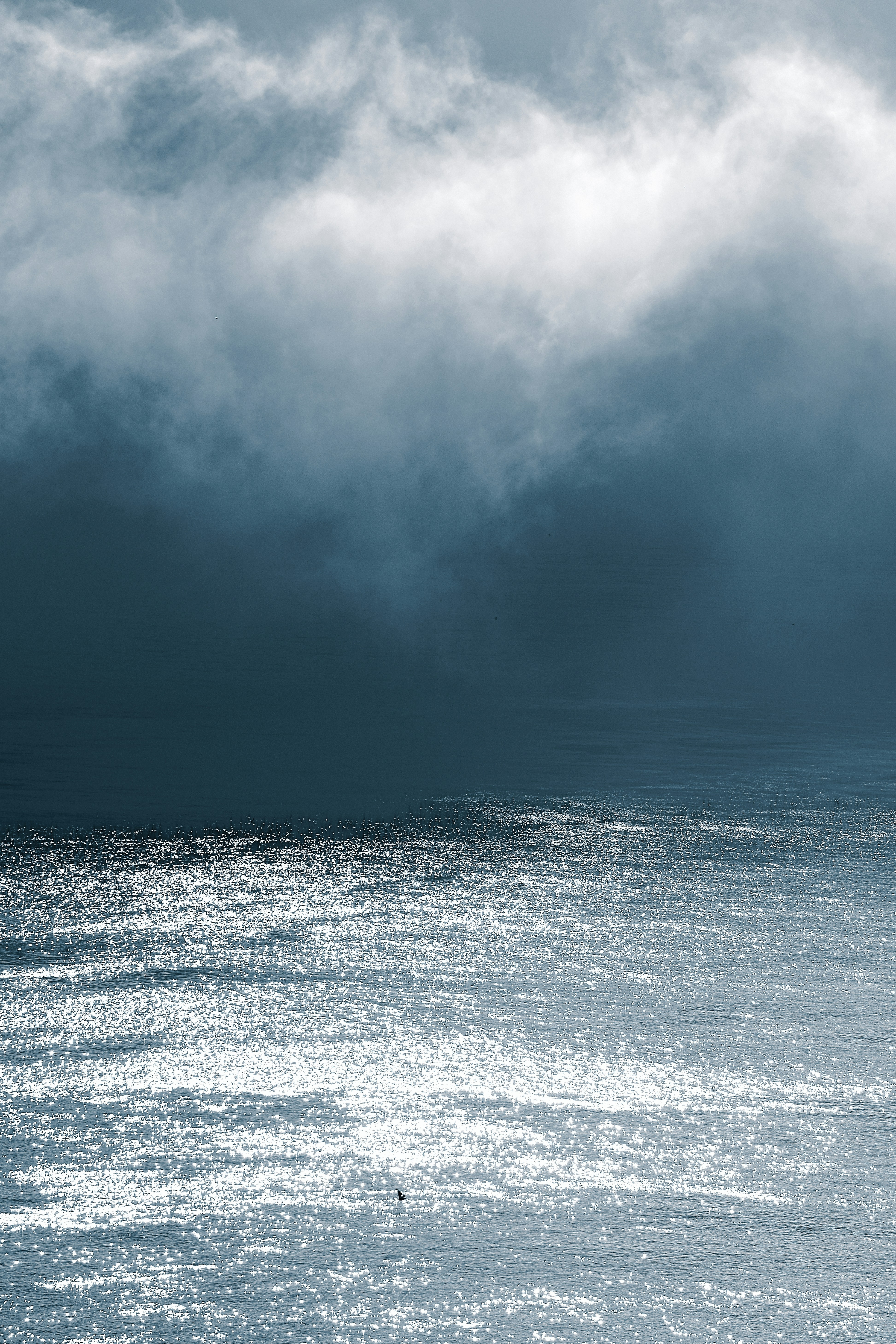 Sunlight reflecting on dark blue water beneath a heavy bank of low clouds