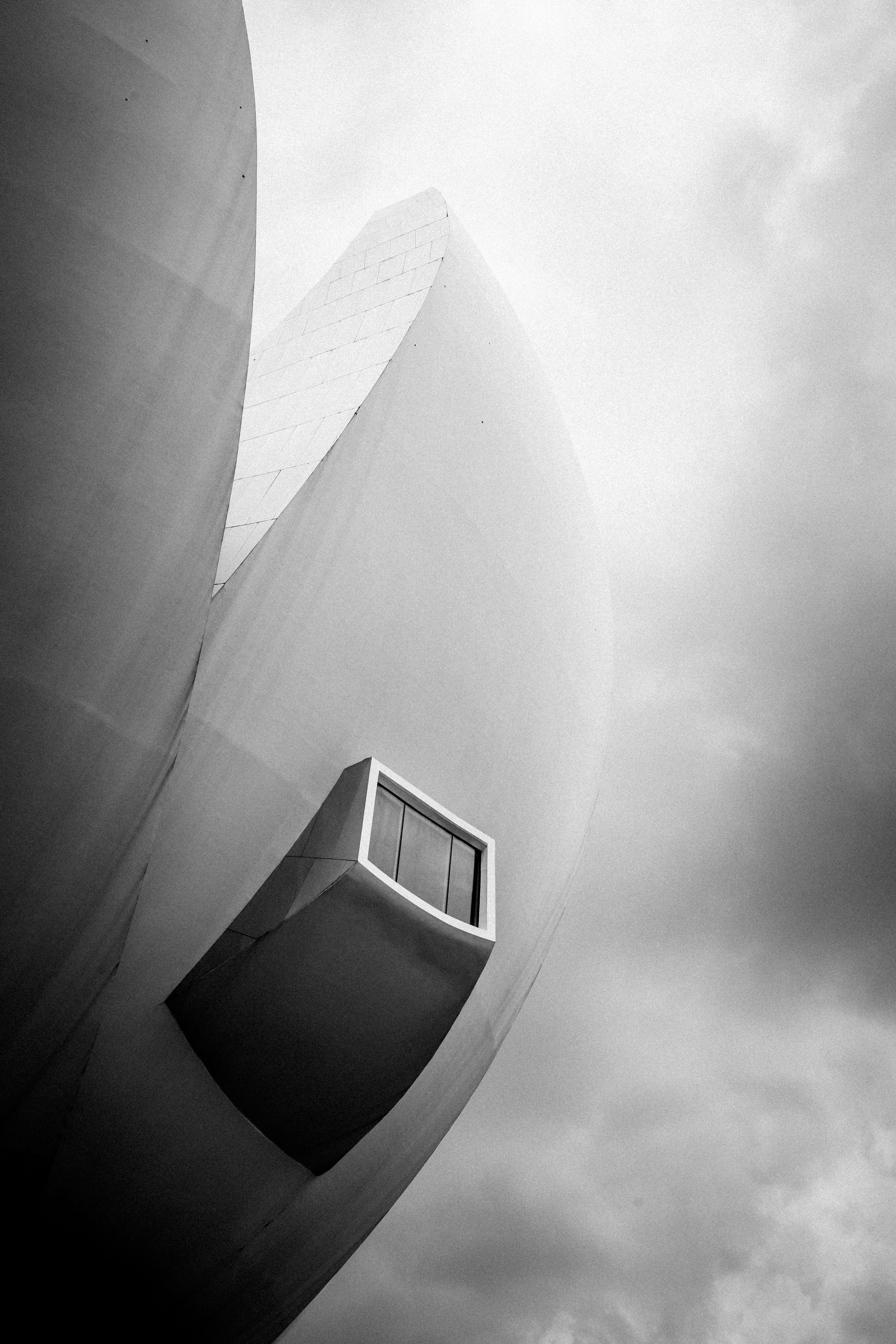 Une vue en noir et blanc d’une façade incurvée de bâtiment blanc avec une fenêtre sur un ciel nuageux