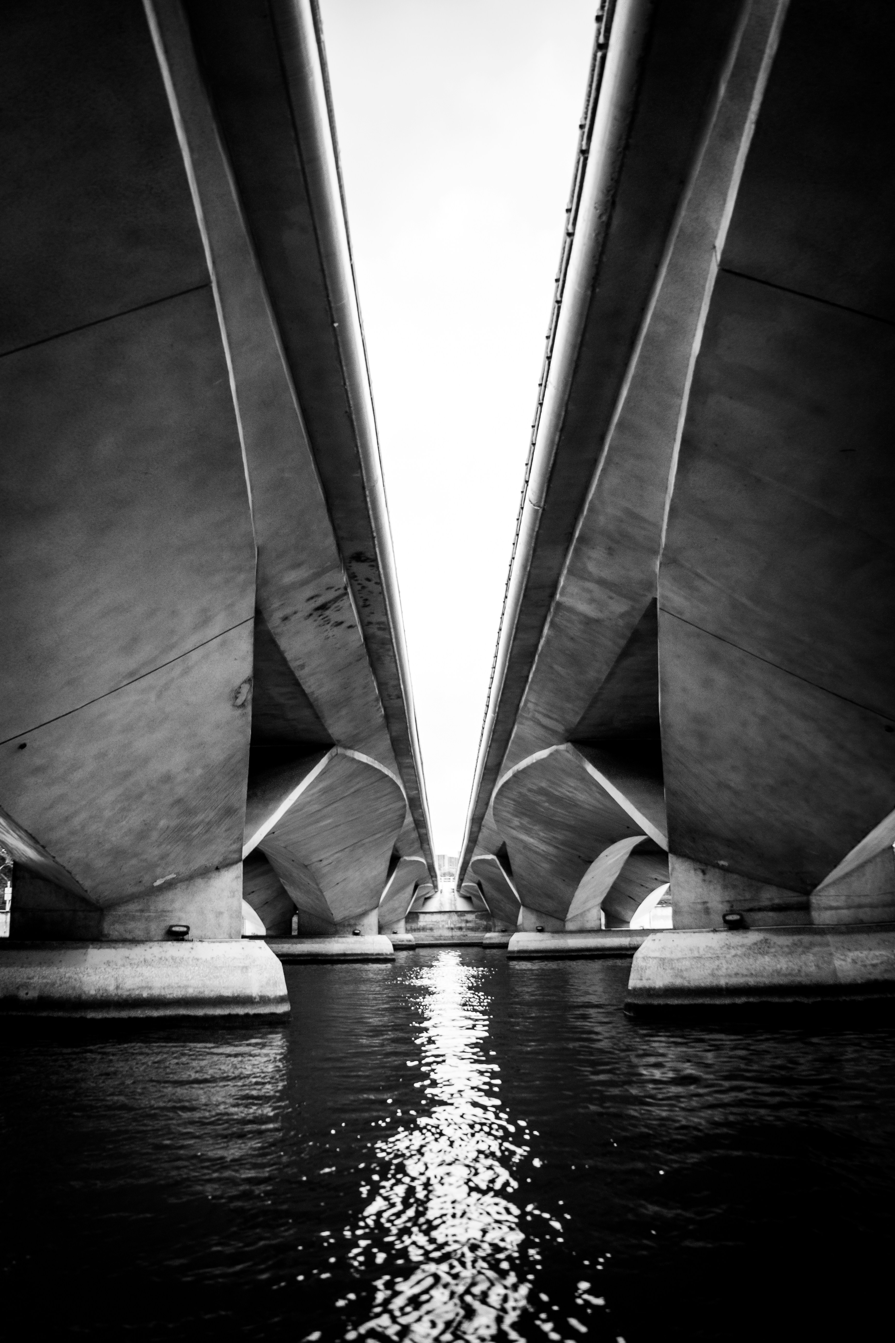 Le dessous de deux ponts parallèles en béton au-dessus d’une eau sombre en noir et blanc