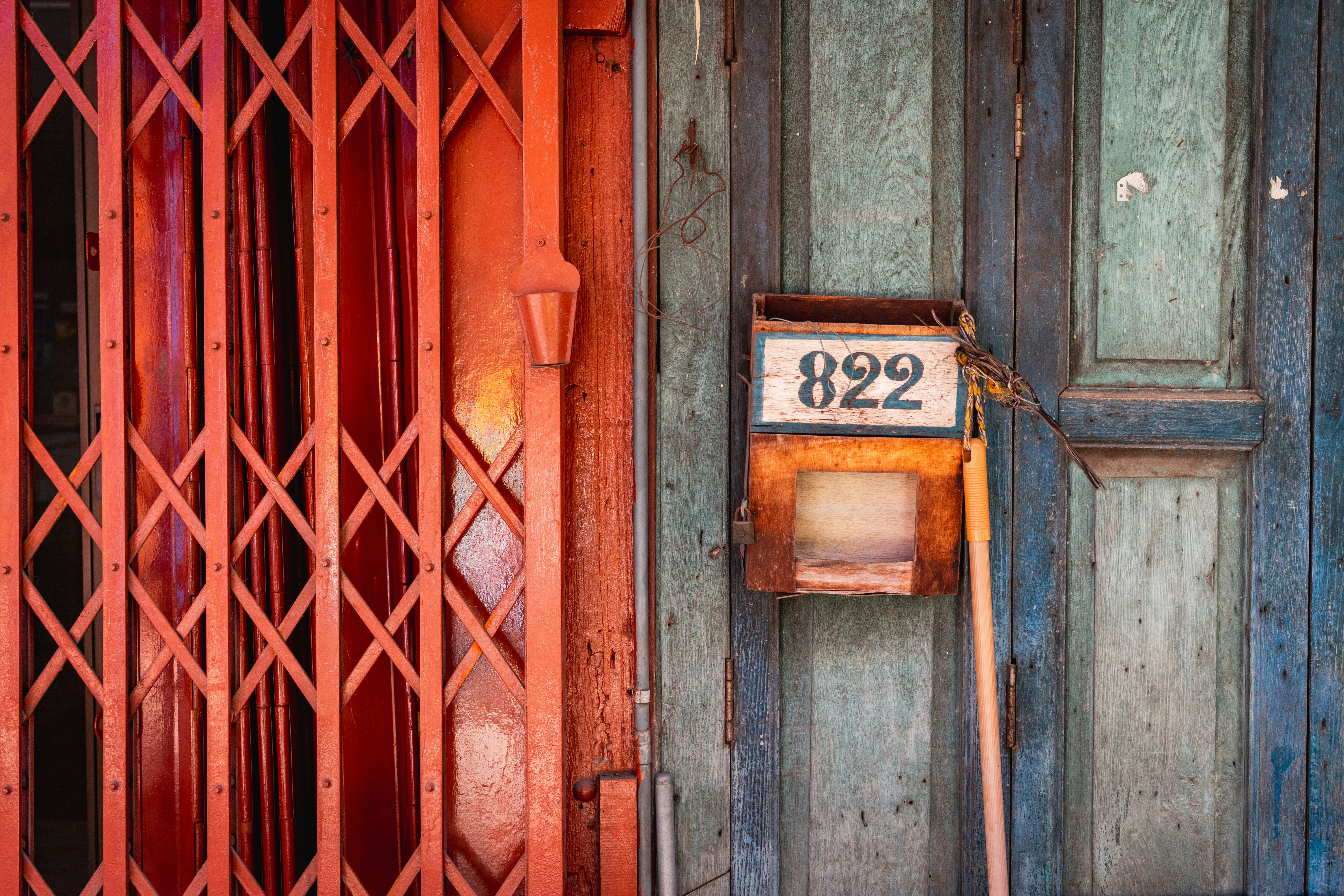 Un portail accordéon en métal rouge à côté d’une porte en bois usé avec une boîte aux lettres indiquant 822 à Bangkok