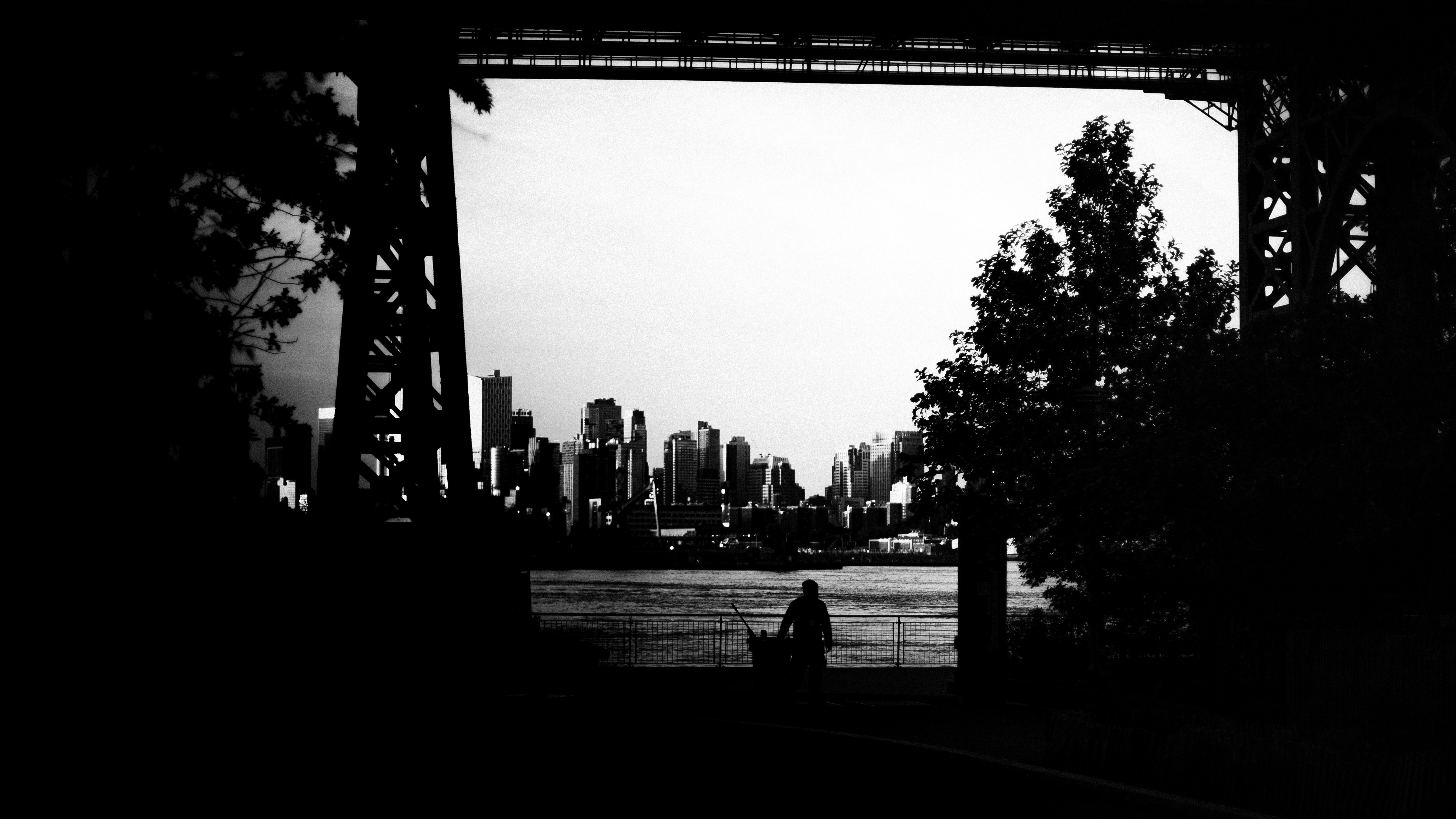 A silhouette of a person walking along a waterfront in New York with the city skyline beyond