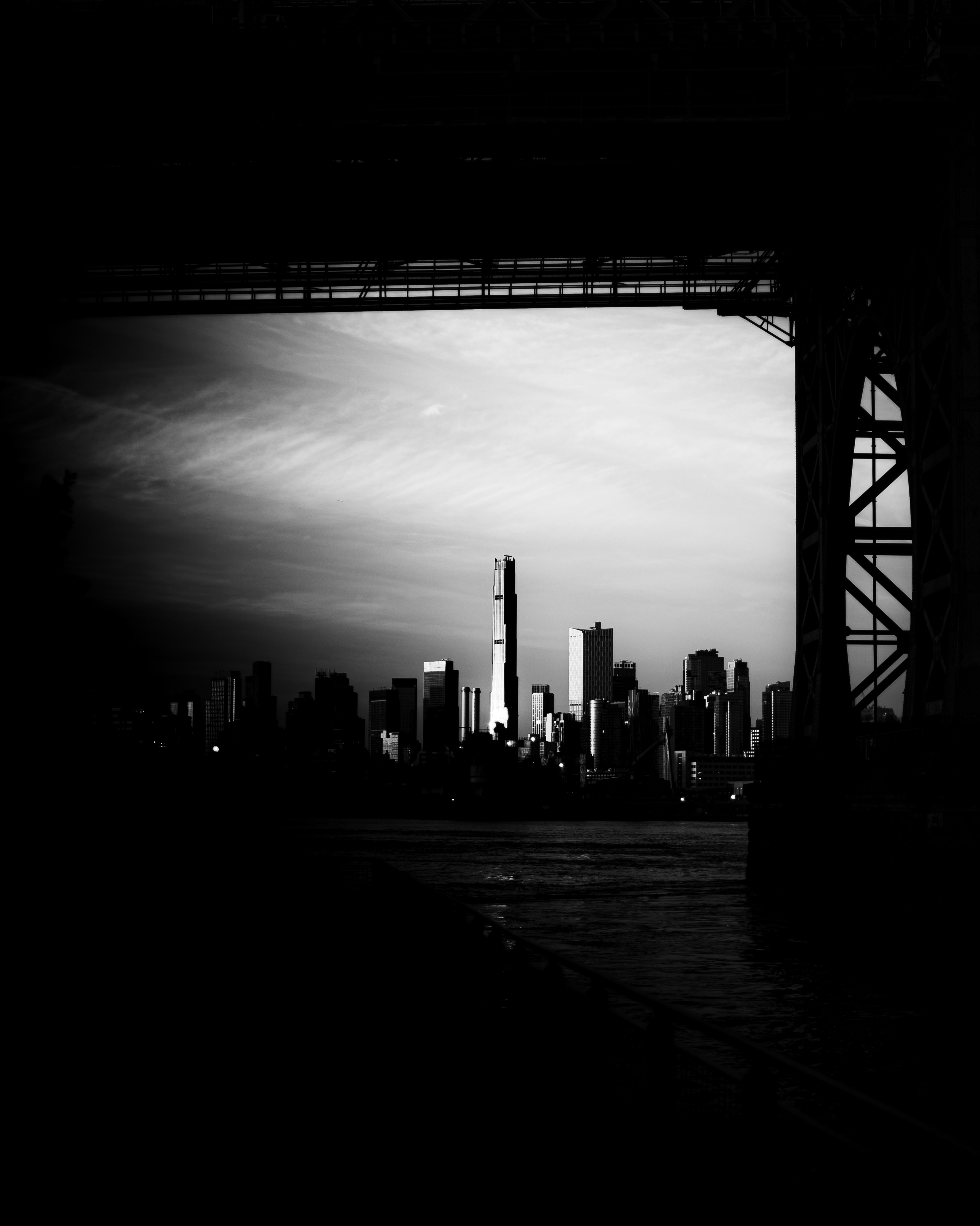 A black and white silhouette of the New York City skyline framed by bridge supports