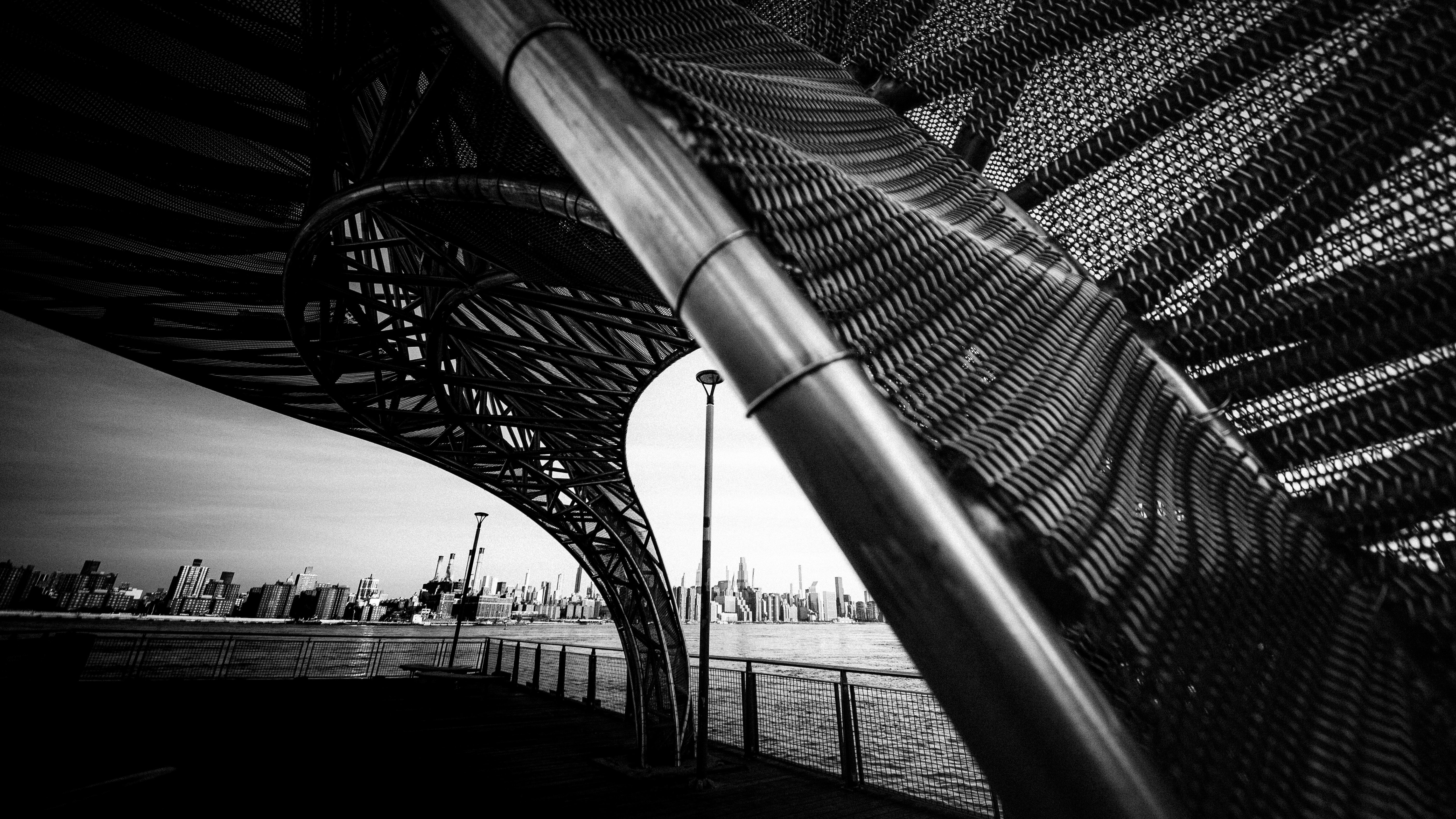A black and white view of a curved metal structure overlooking a distant city skyline