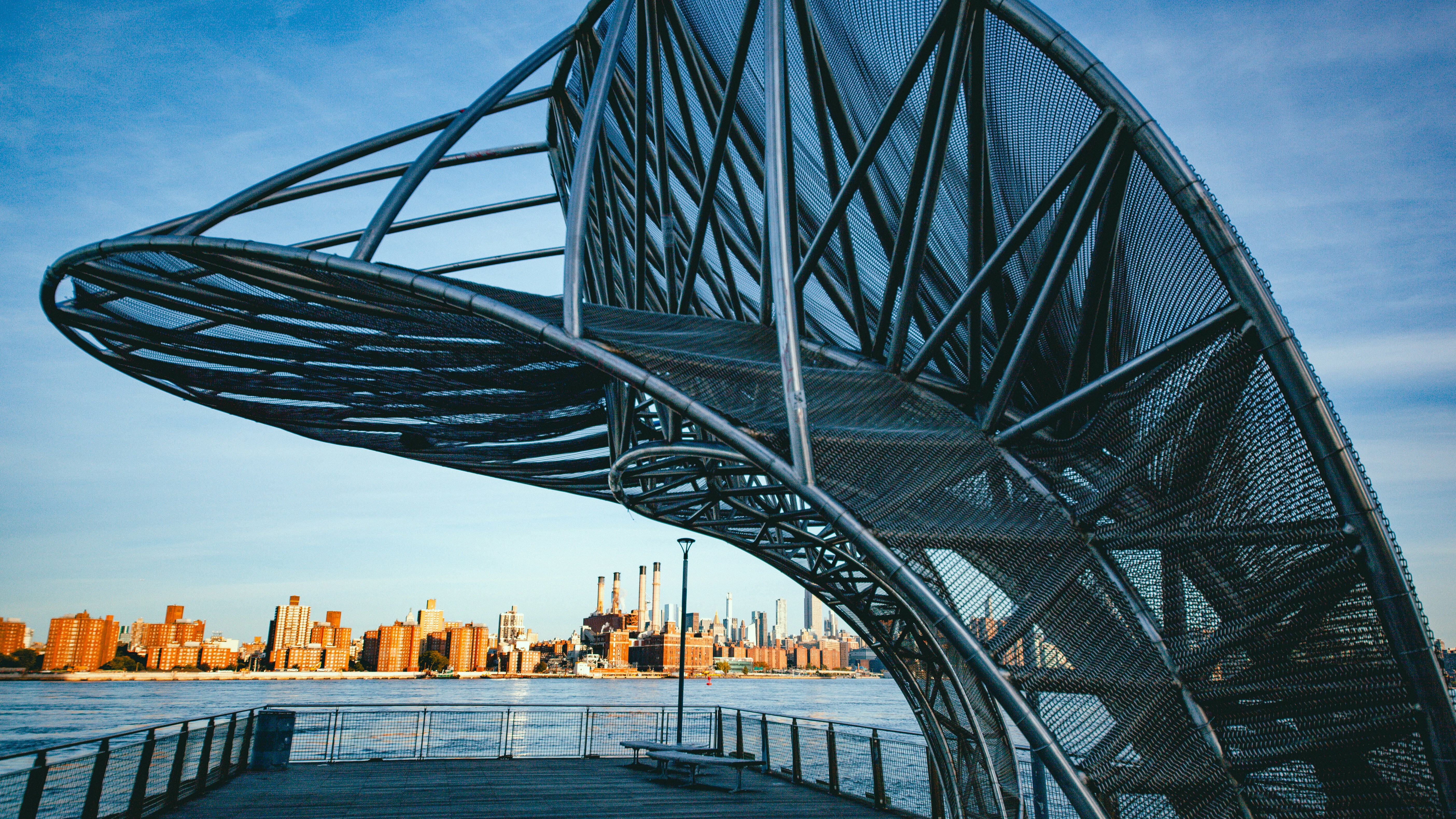A large metal sculpture on a pier overlooking the Manhattan skyline in New York