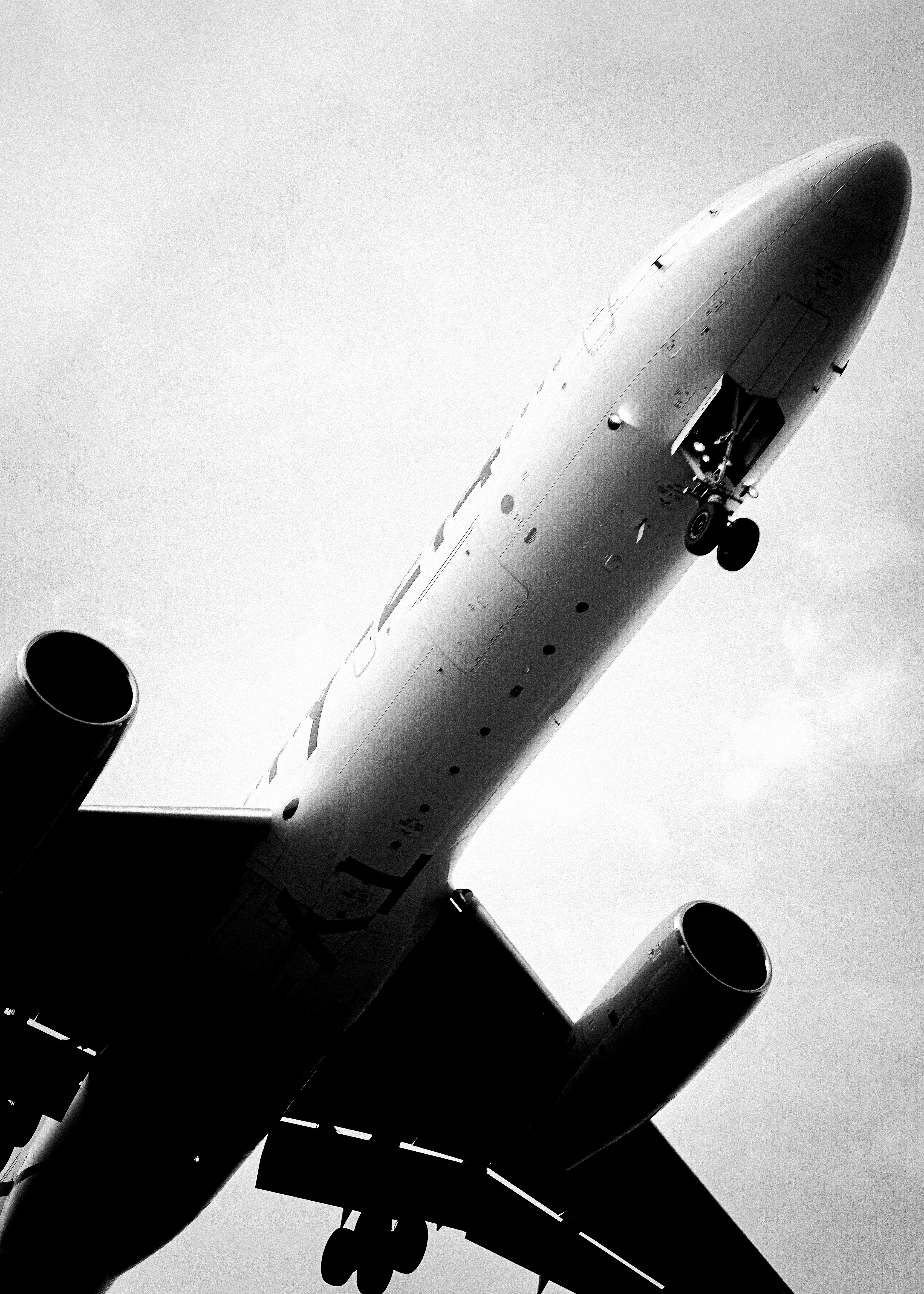 A black and white low angle view of a passenger airplane with landing gear extended