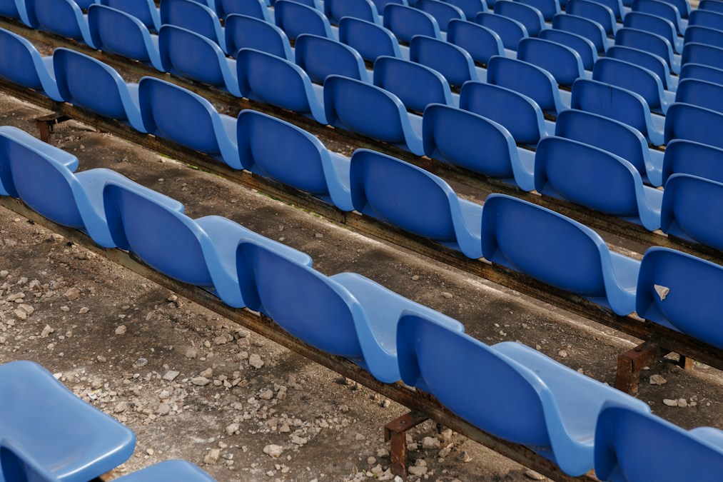 Rangées de sièges bleus vides sur une tribune de stade en béton, sans aucun spectateur