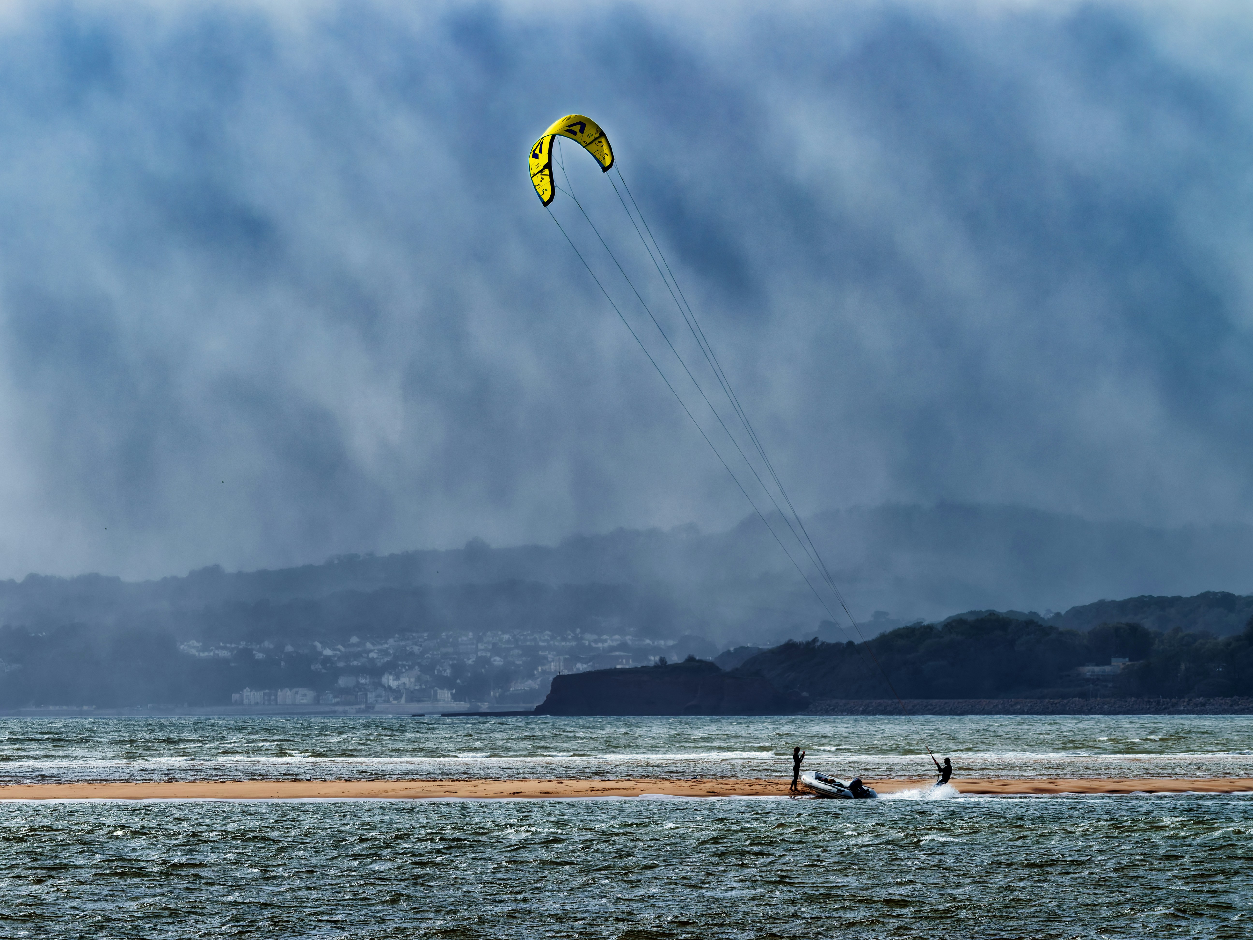 A kite surfer on a sandbar in the Exe Estuary with a yellow kite overhead