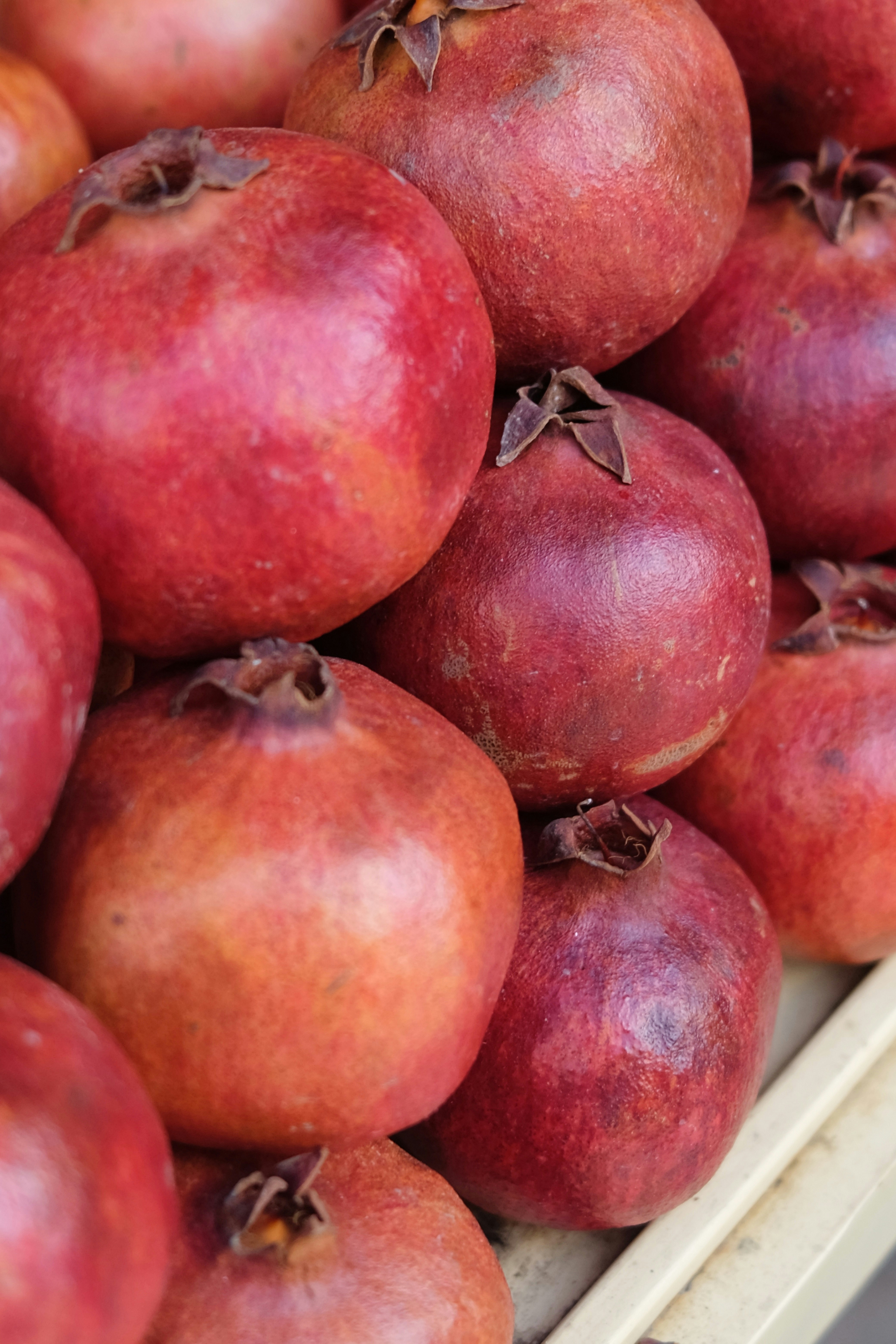 A close-up of a pile of ripe red pomegranates with textured skins