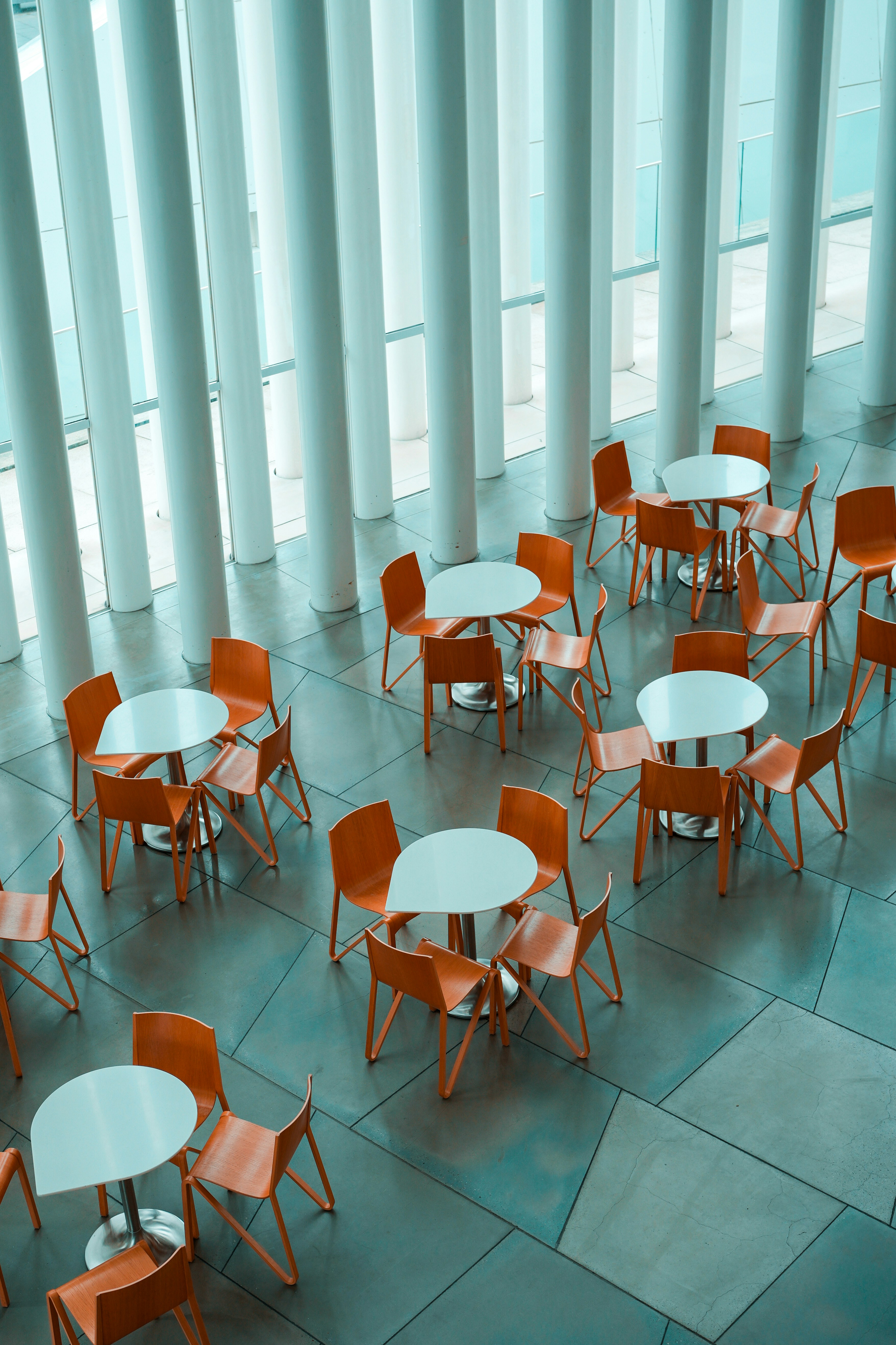 An aerial view of white tables and orange chairs in a modern sunlit atrium