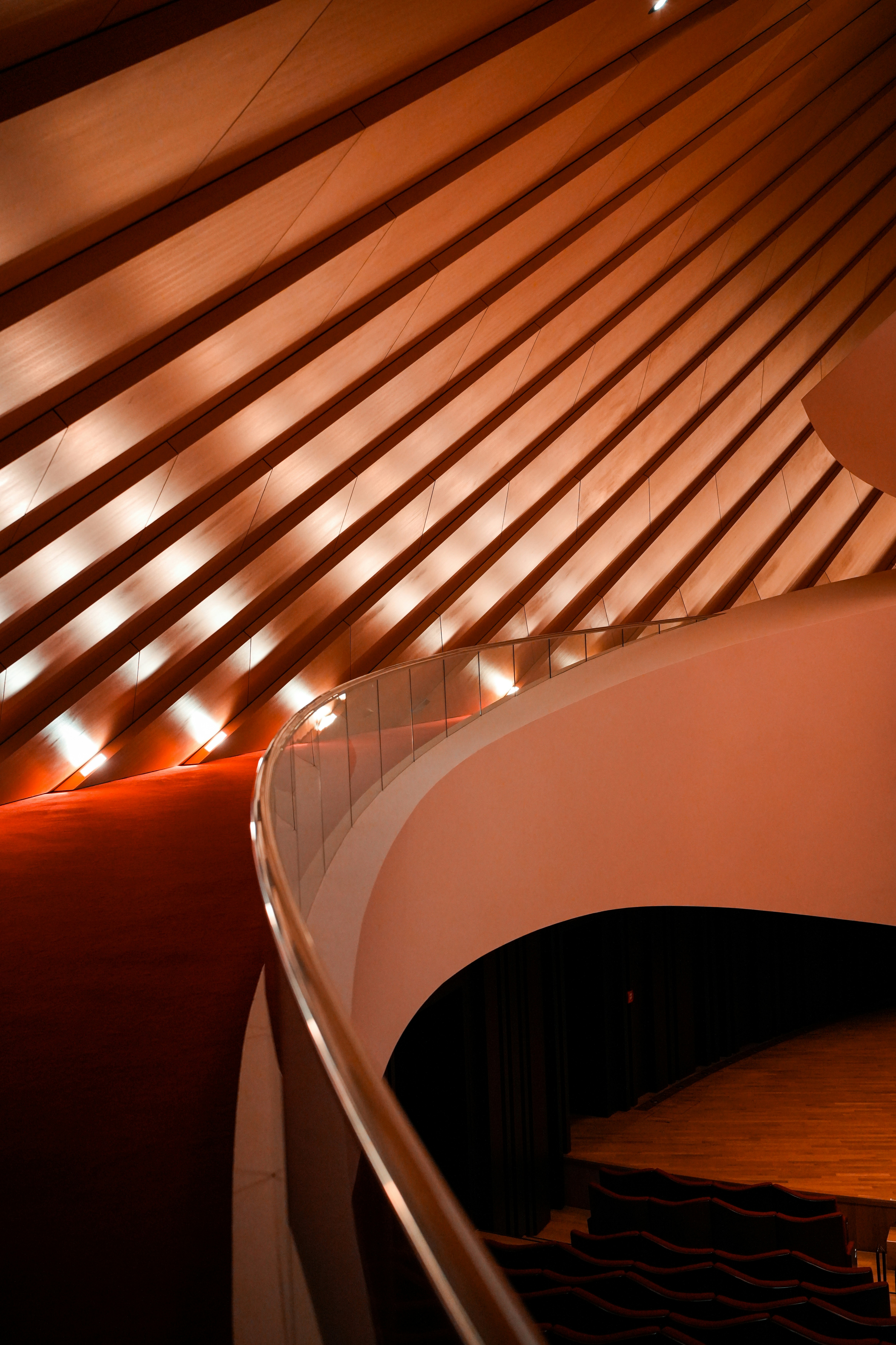 A curved glass railing overlooking a theater interior with wooden slatted walls and rows of seats