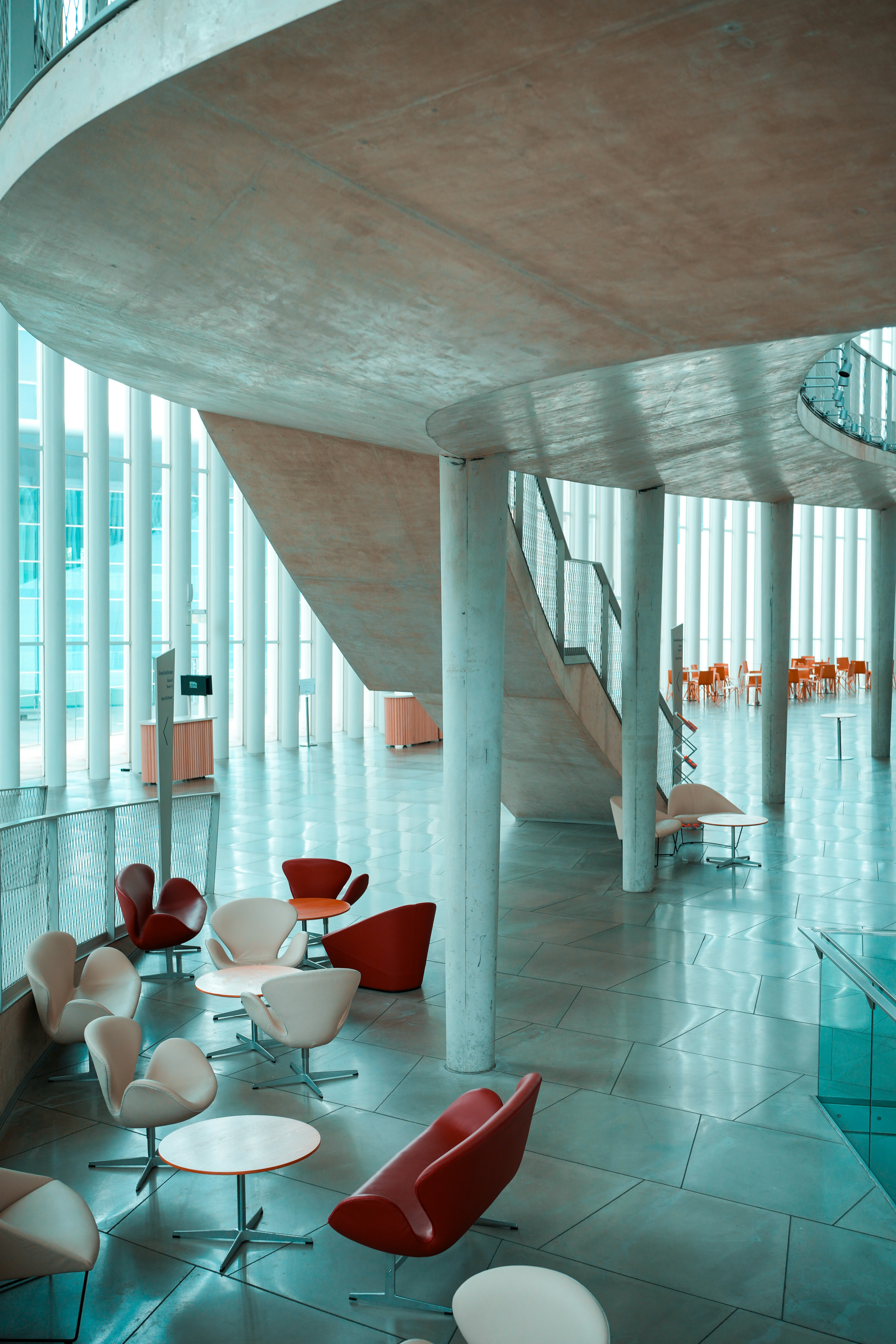 Modern lounge area with red and white chairs and small tables under a concrete staircase