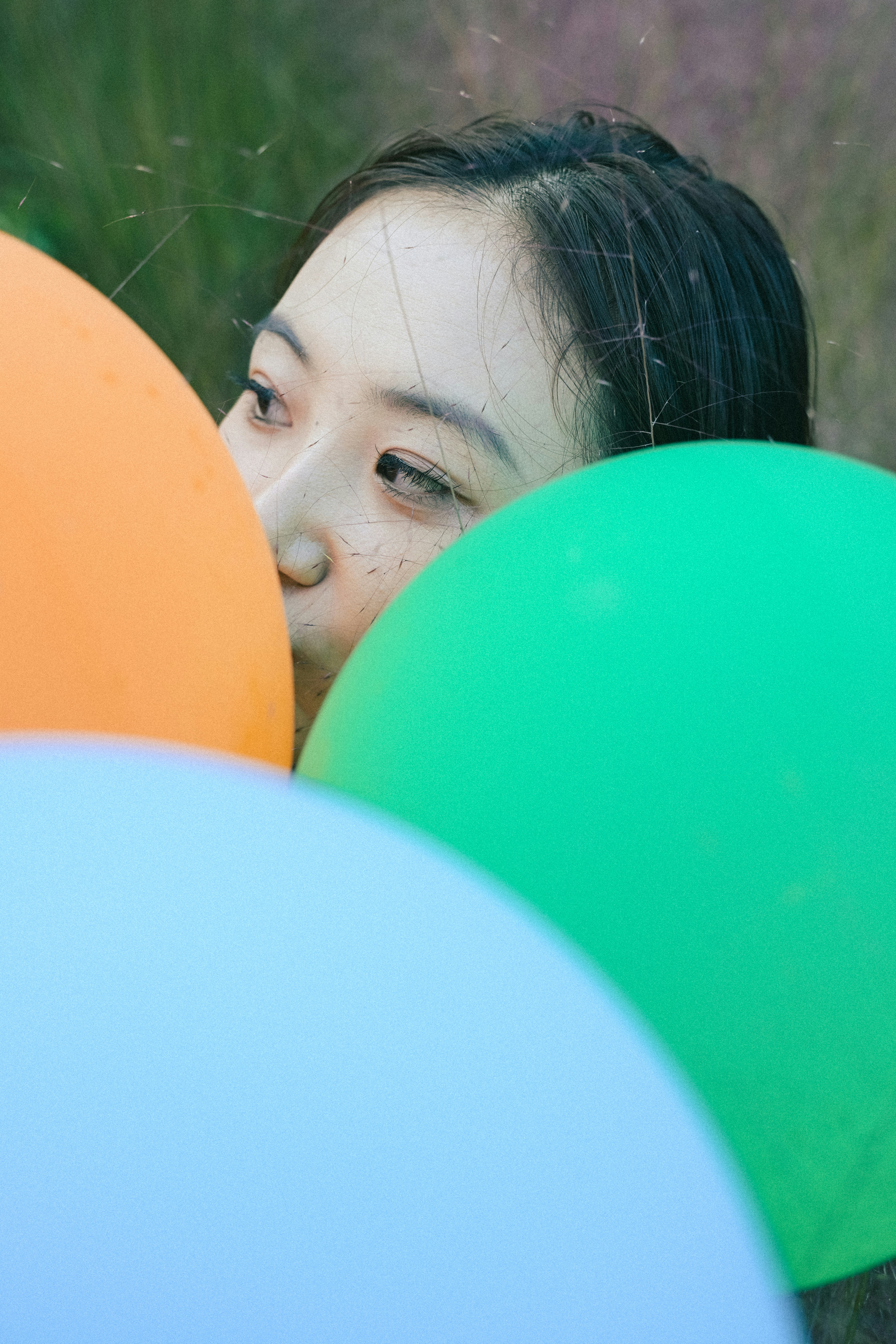 A woman peeking from behind bright orange, green, and blue balloons in a grassy field