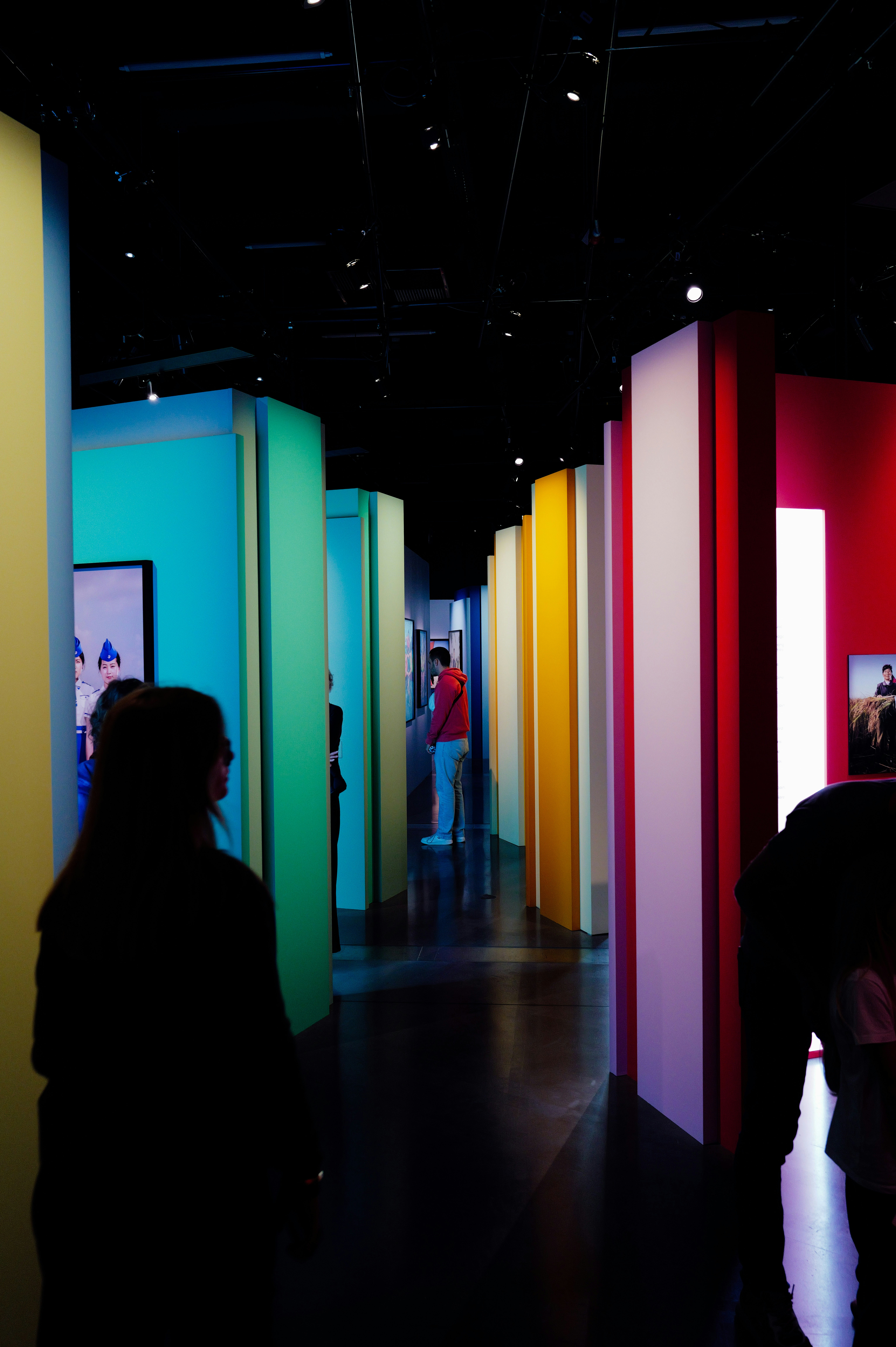 Des gens traversant une galerie aux murs colorés et illuminés et encadrés de photographies