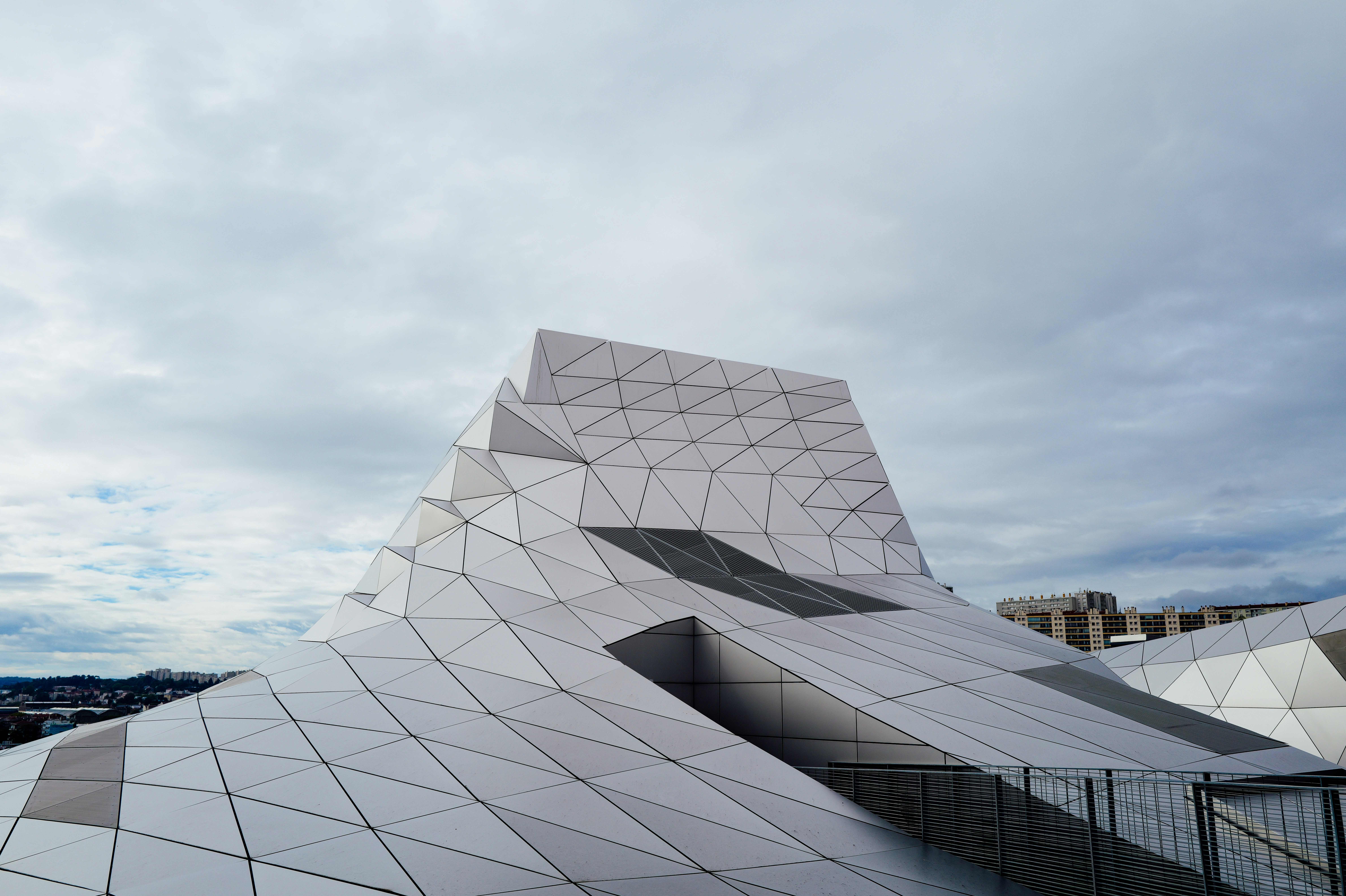 Un bâtiment moderne avec une façade géométrique en panneaux blancs sous un ciel nuageux