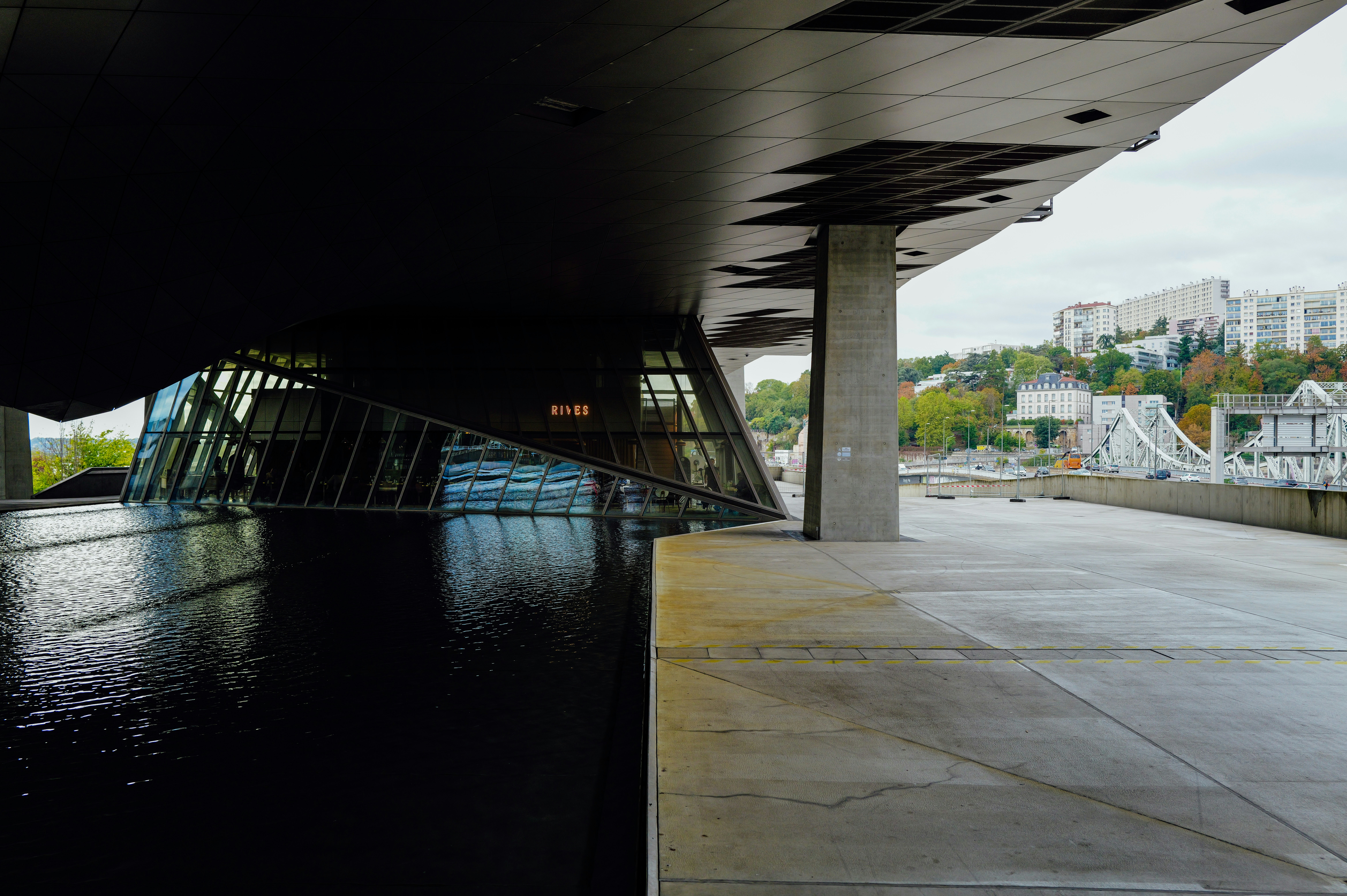 Un bâtiment moderne avec un grand pilier en béton et une piscine réfléchissante à Lyon