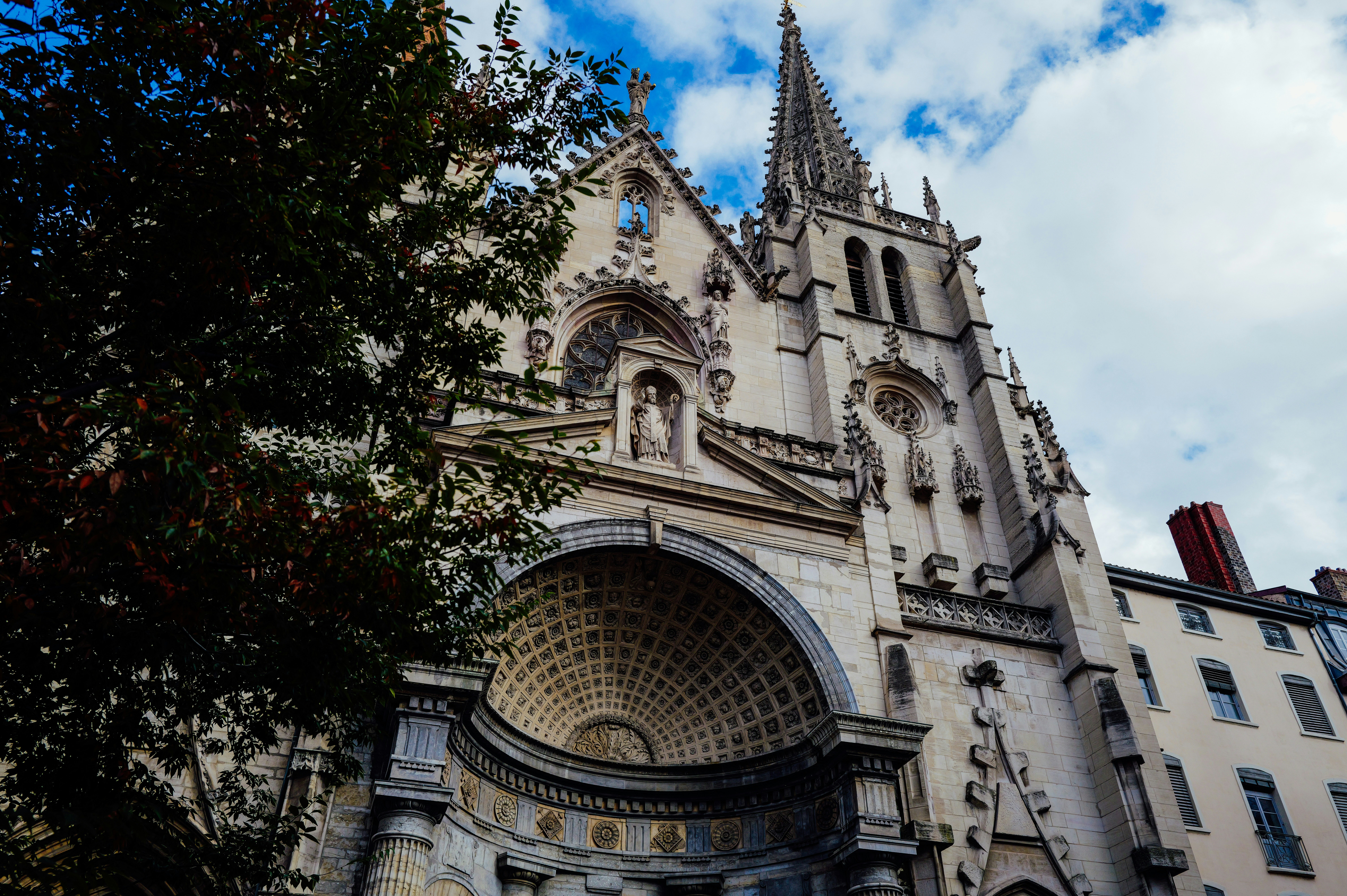 La façade ornée en pierre de l’église Saint-Nizier à Lyon sous un ciel bleu nuageux