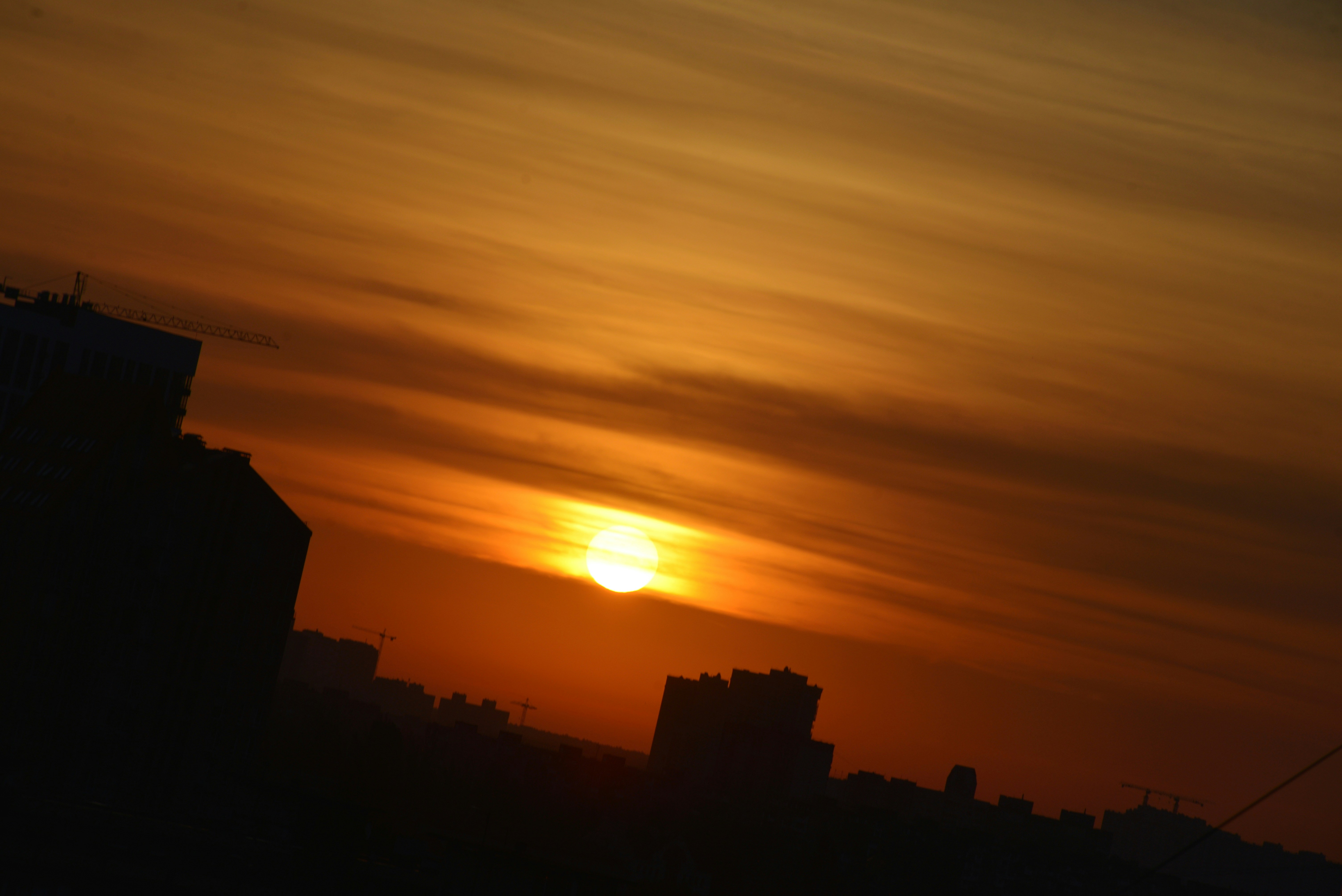 Des bâtiments citadins en silhouette sur un ciel orange vif avec un soleil bas