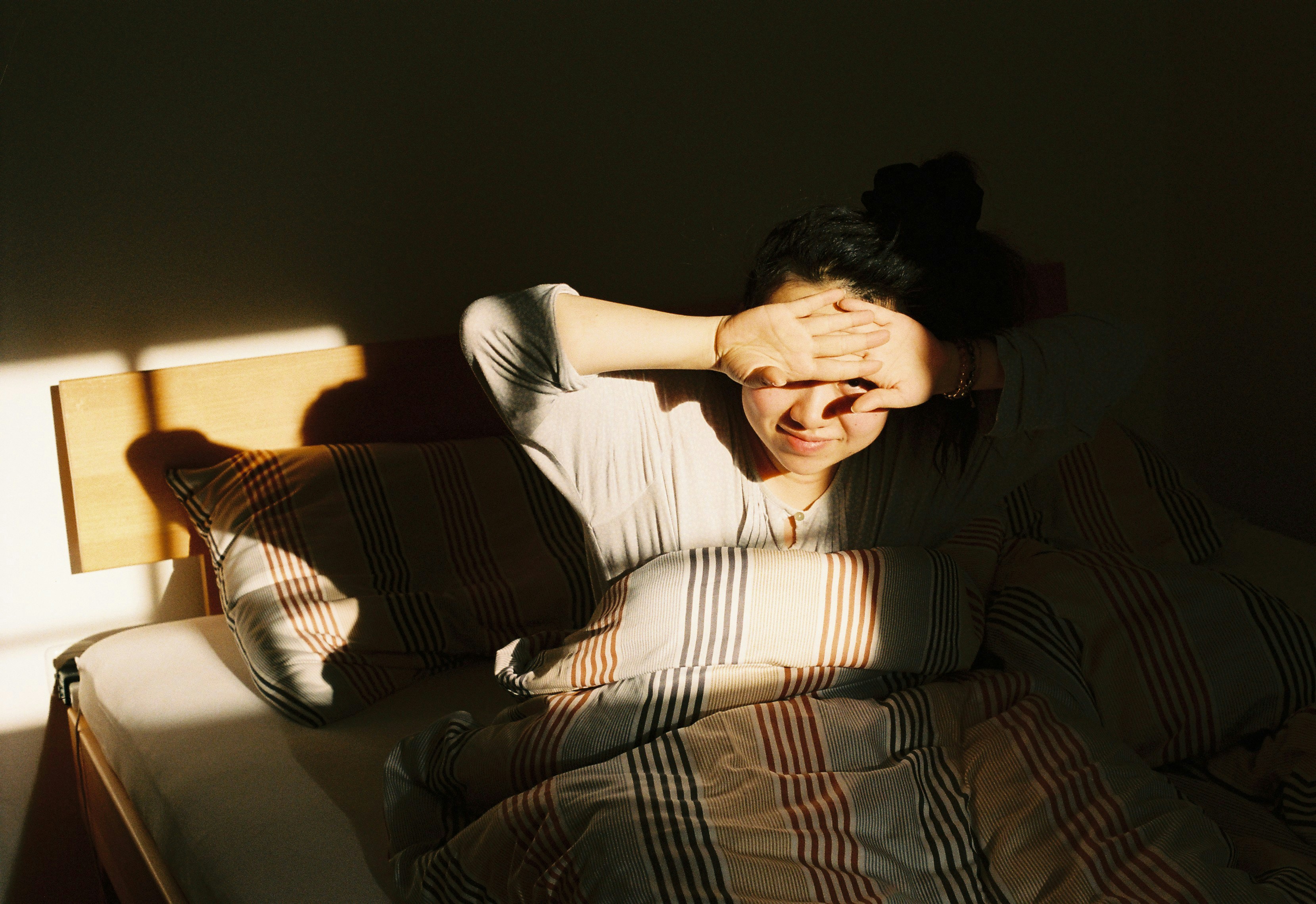 A woman in bed shielding her eyes from bright morning light in a bedroom