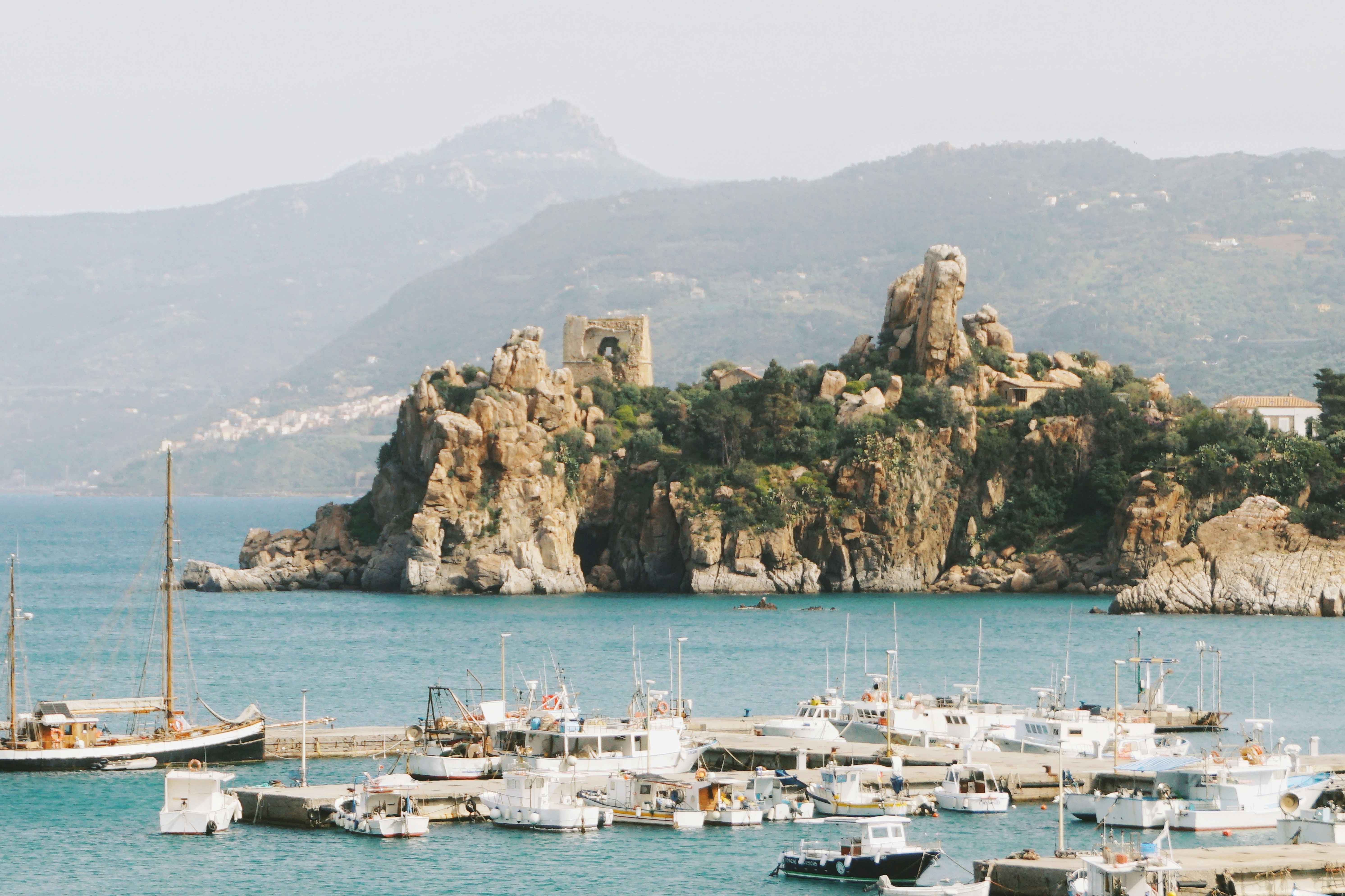Fishing boats moored at a pier below a rocky coastal cliff in Cefalù