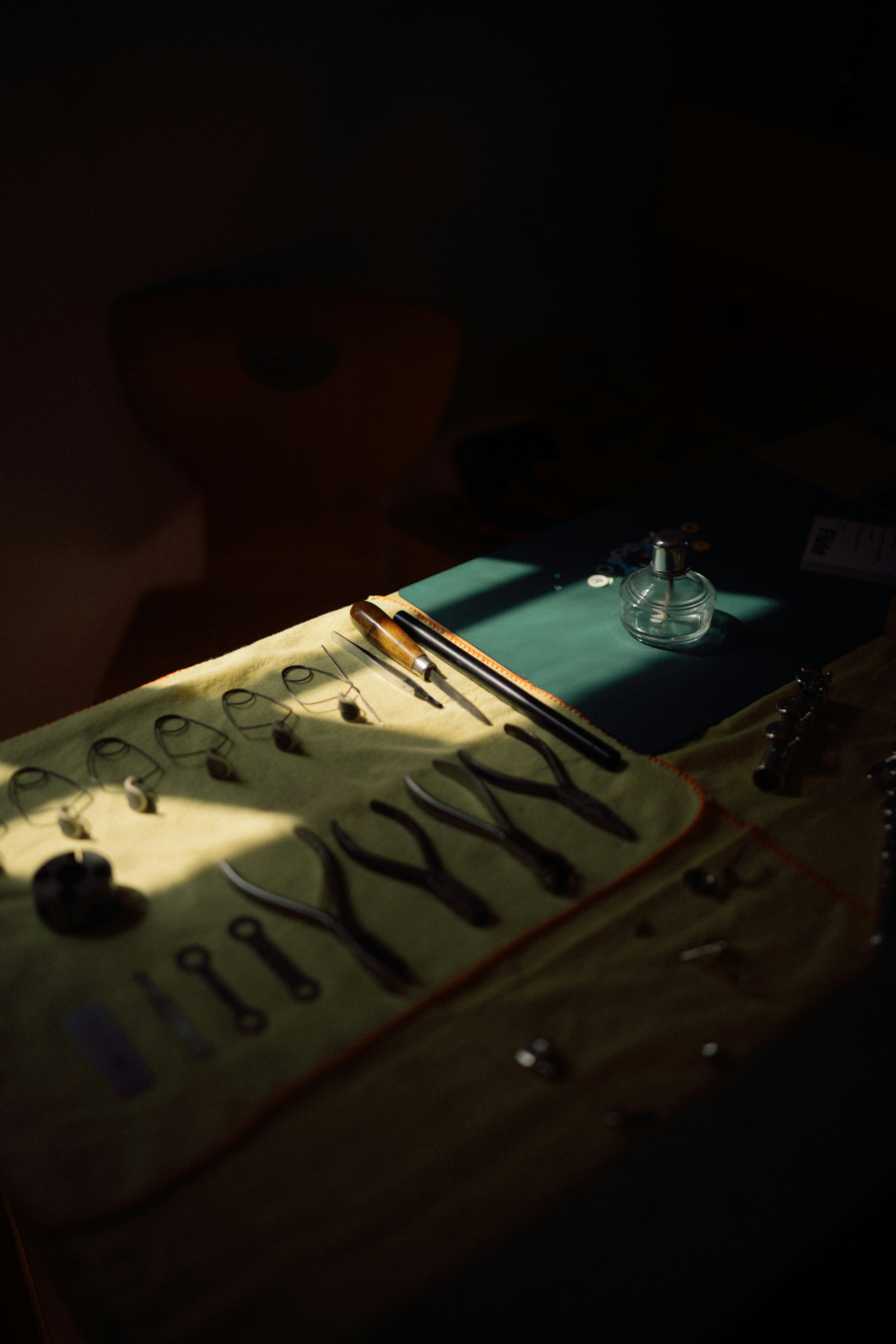 Assorted metal tools and small parts arranged on a yellow cloth in a sunlit workshop