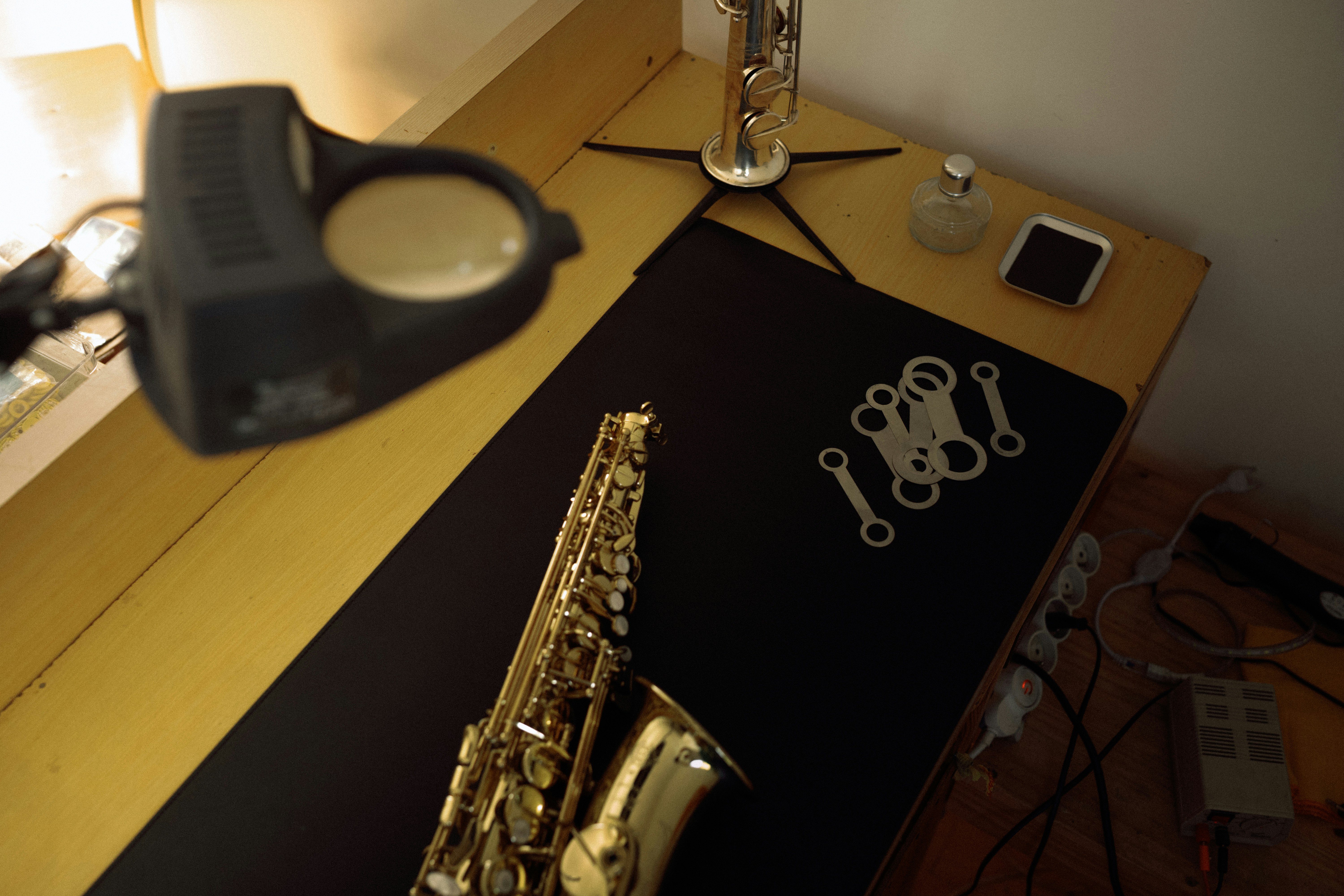 A saxophone and metal parts on a black mat with a magnifying lamp