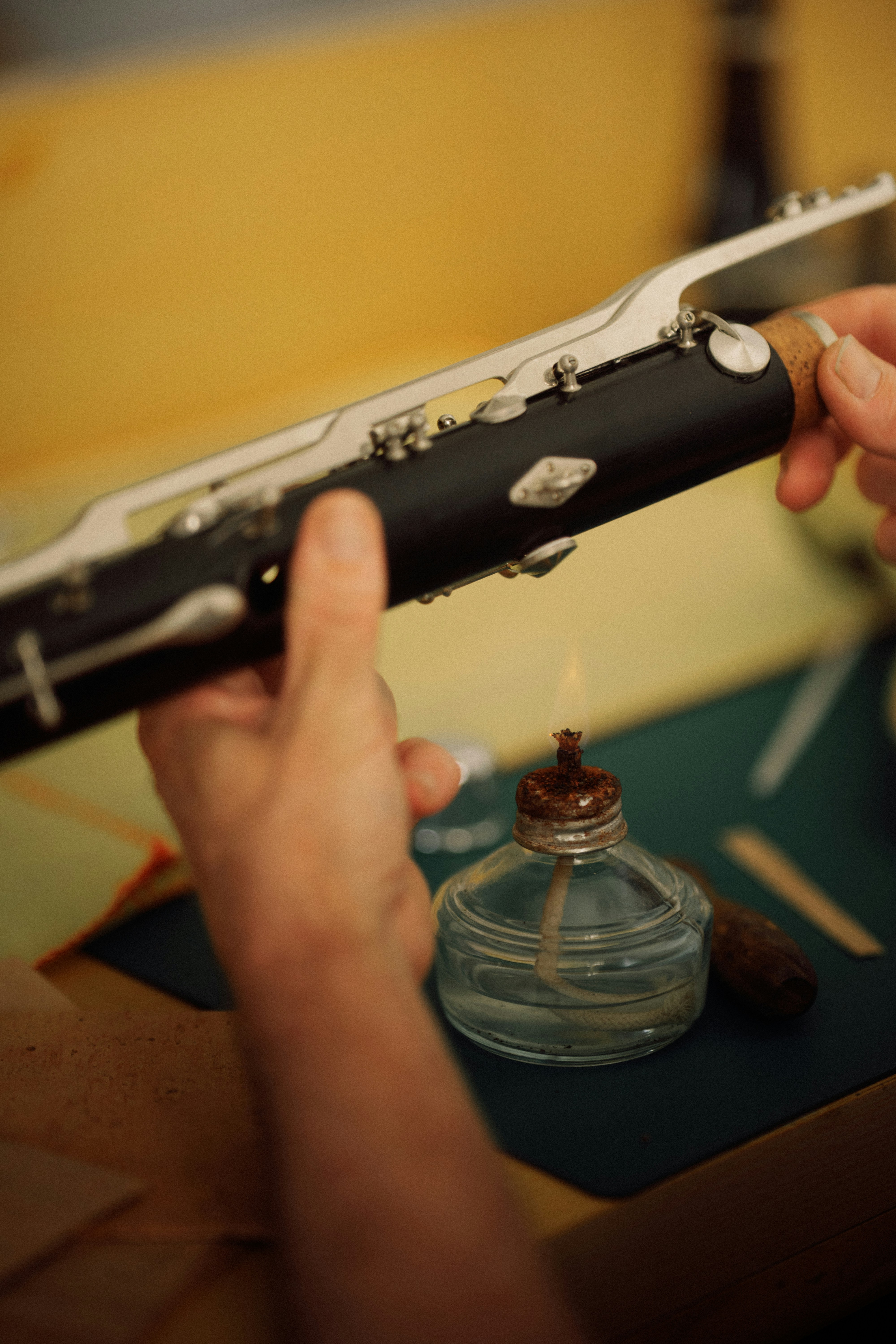 A person heating a clarinet joint over a small glass alcohol lamp
