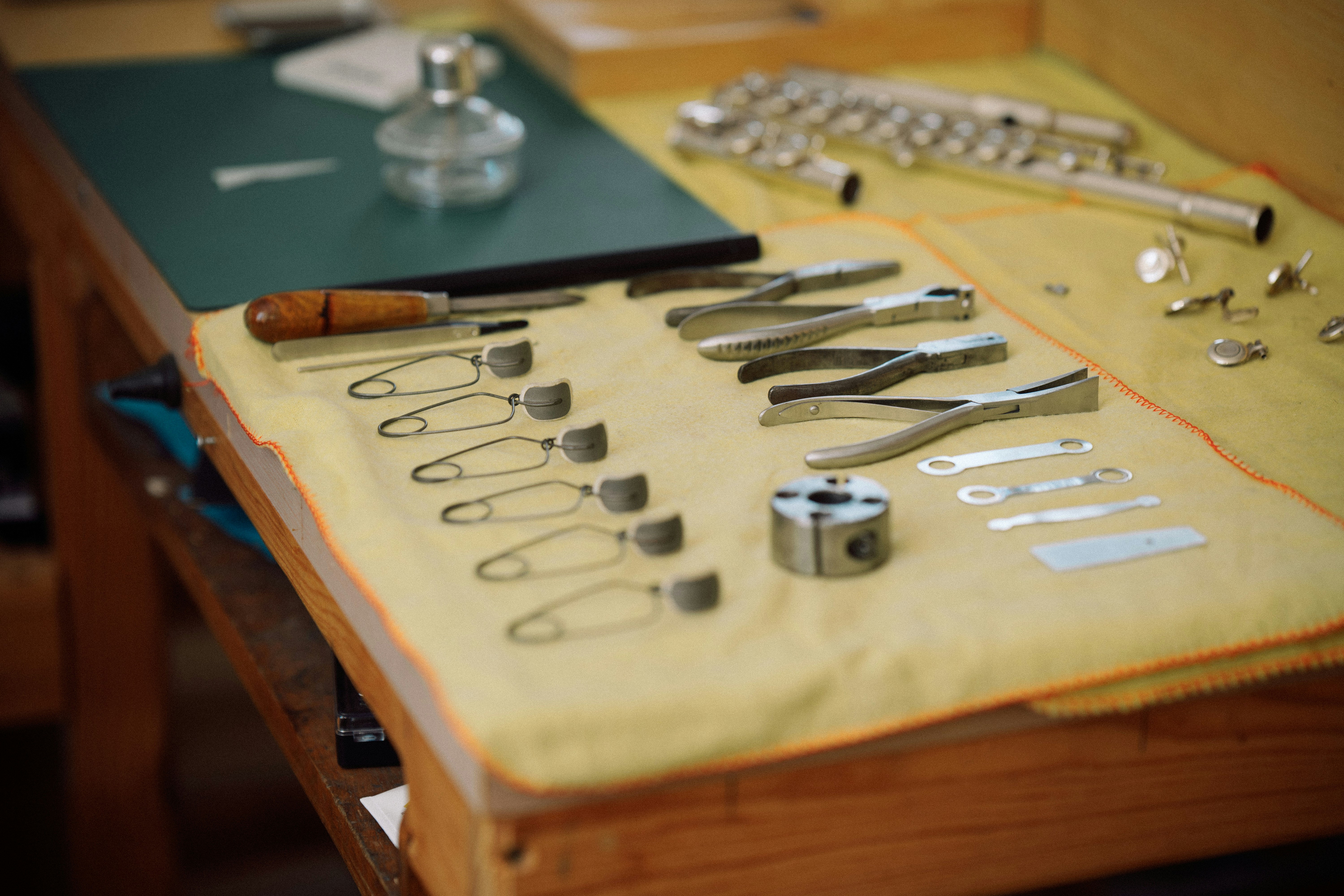 Musical instrument repair tools and disassembled flute parts on a yellow cloth on a wooden workbench
