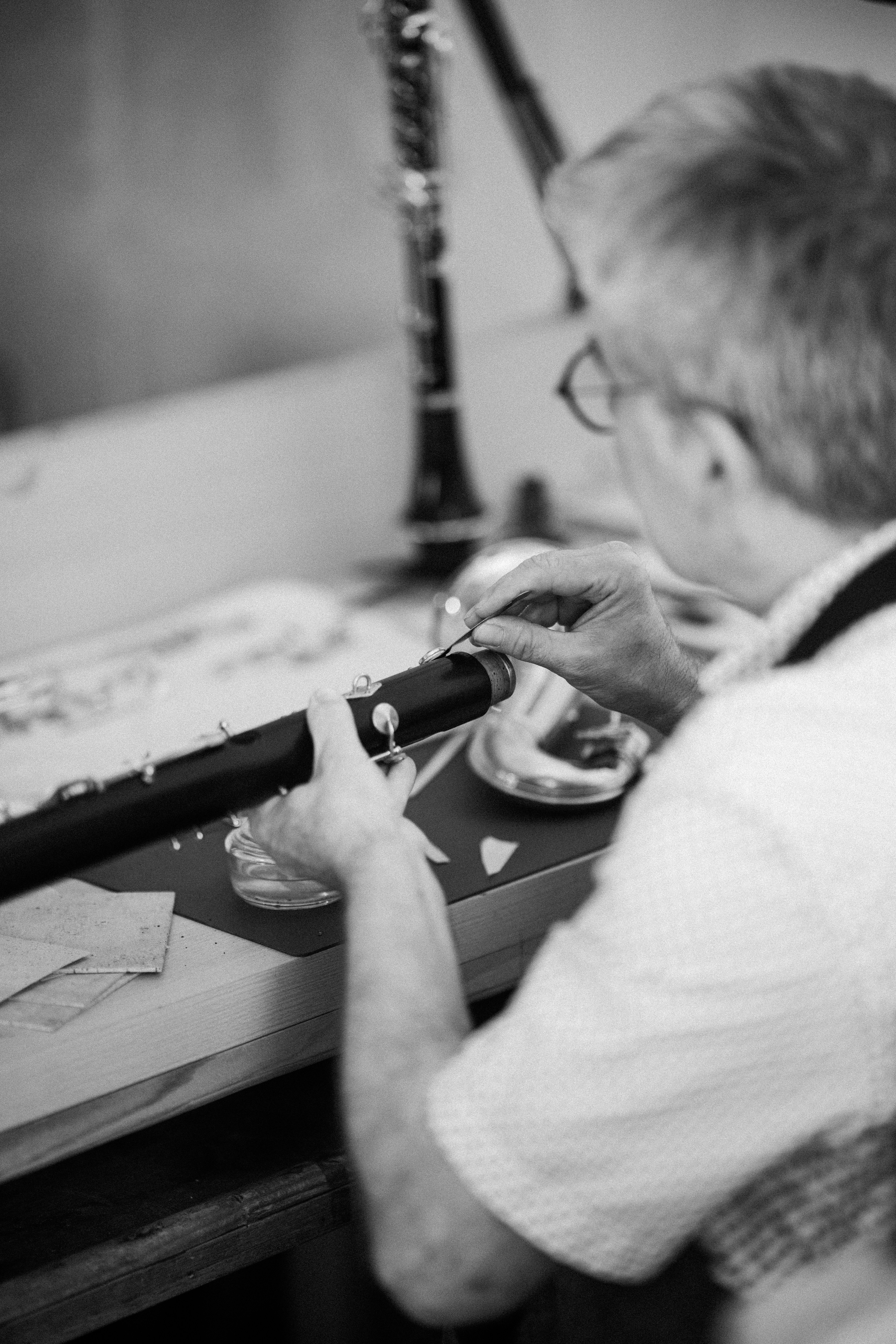 A person in glasses repairing a clarinet with a small tool at a workbench
