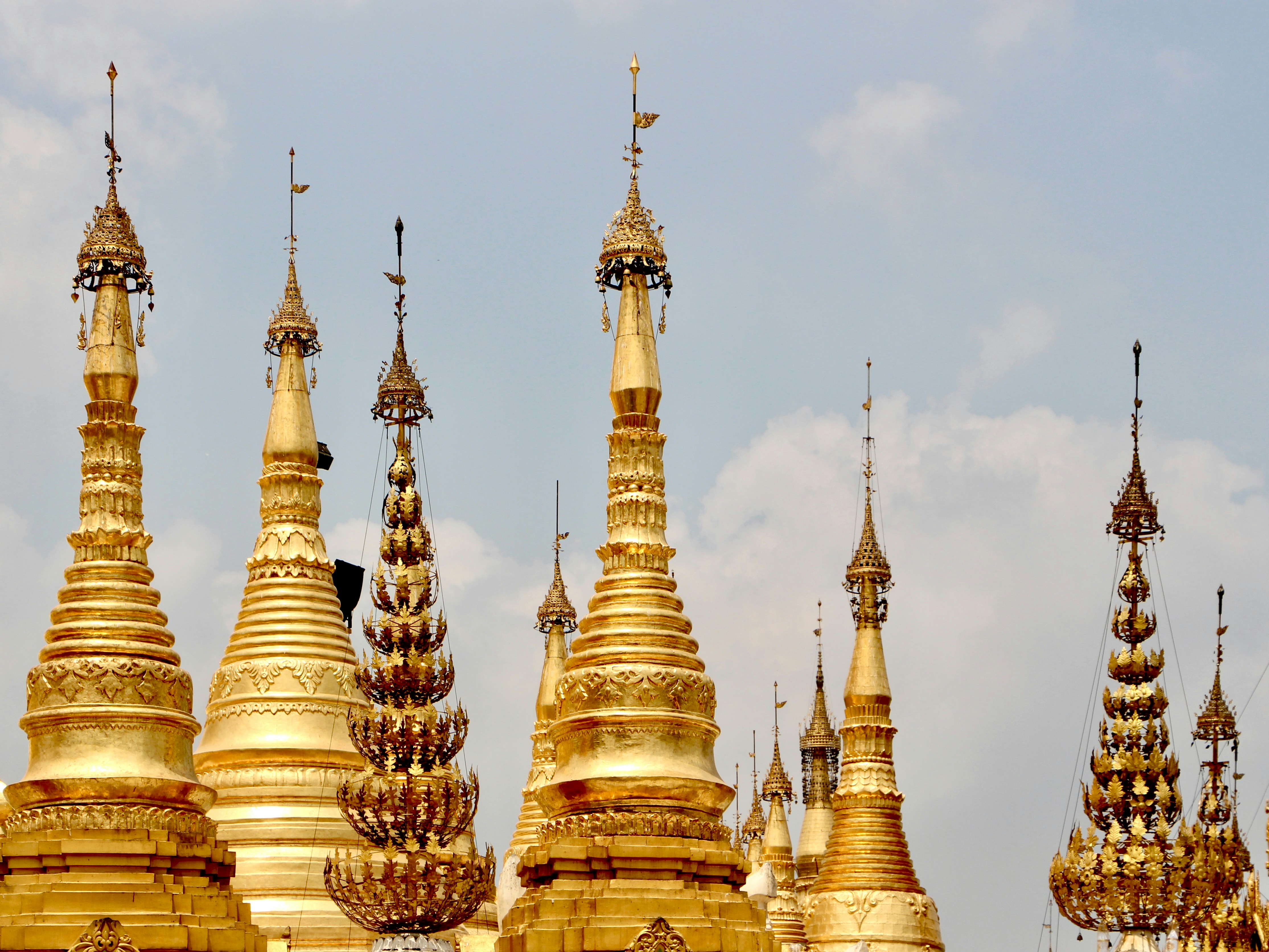 Mehrere goldene Stupas mit kunstvollen Türmen vor einem blassblauen Himmel