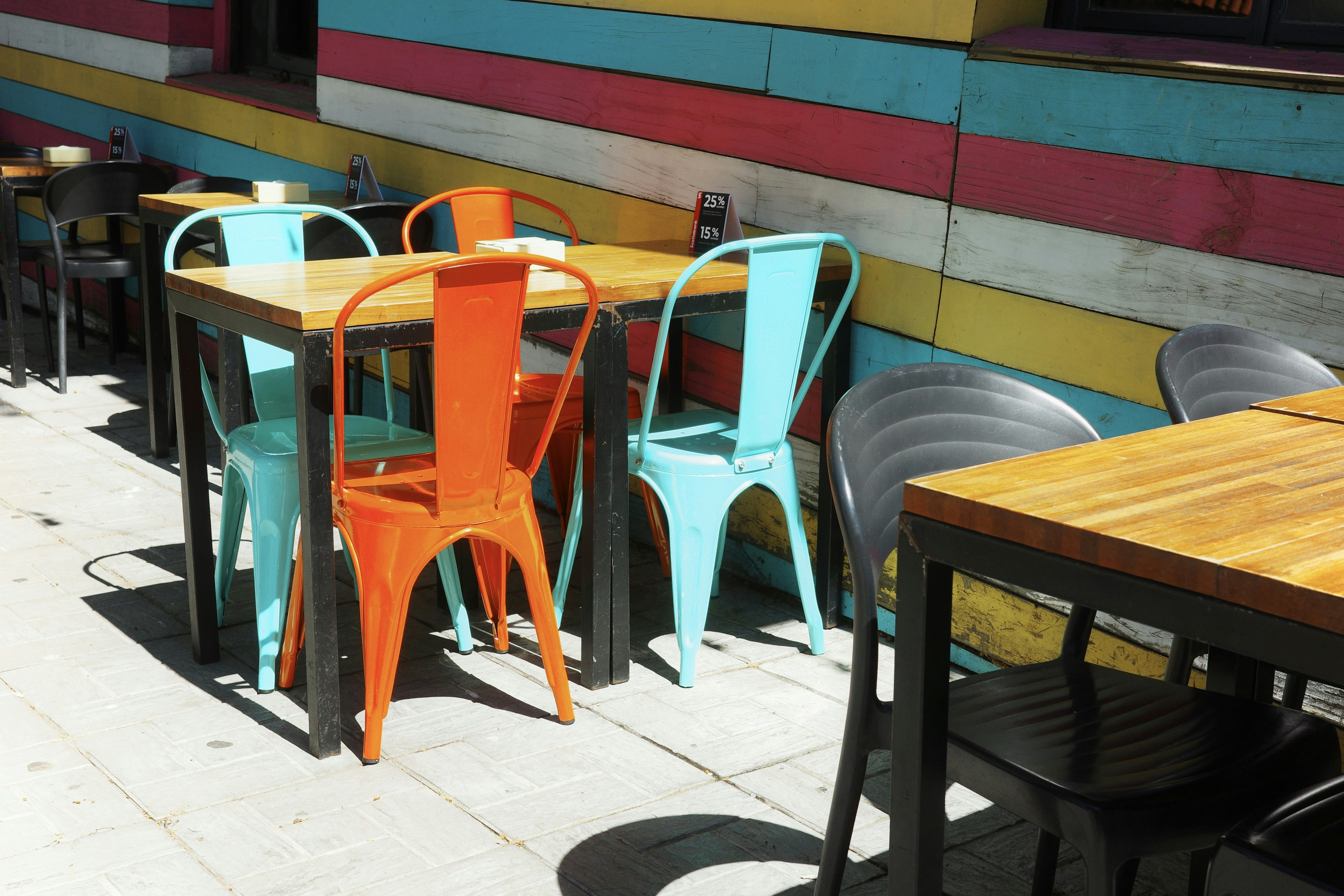 Brightly colored metal chairs at wooden tables against a striped wall on a patio