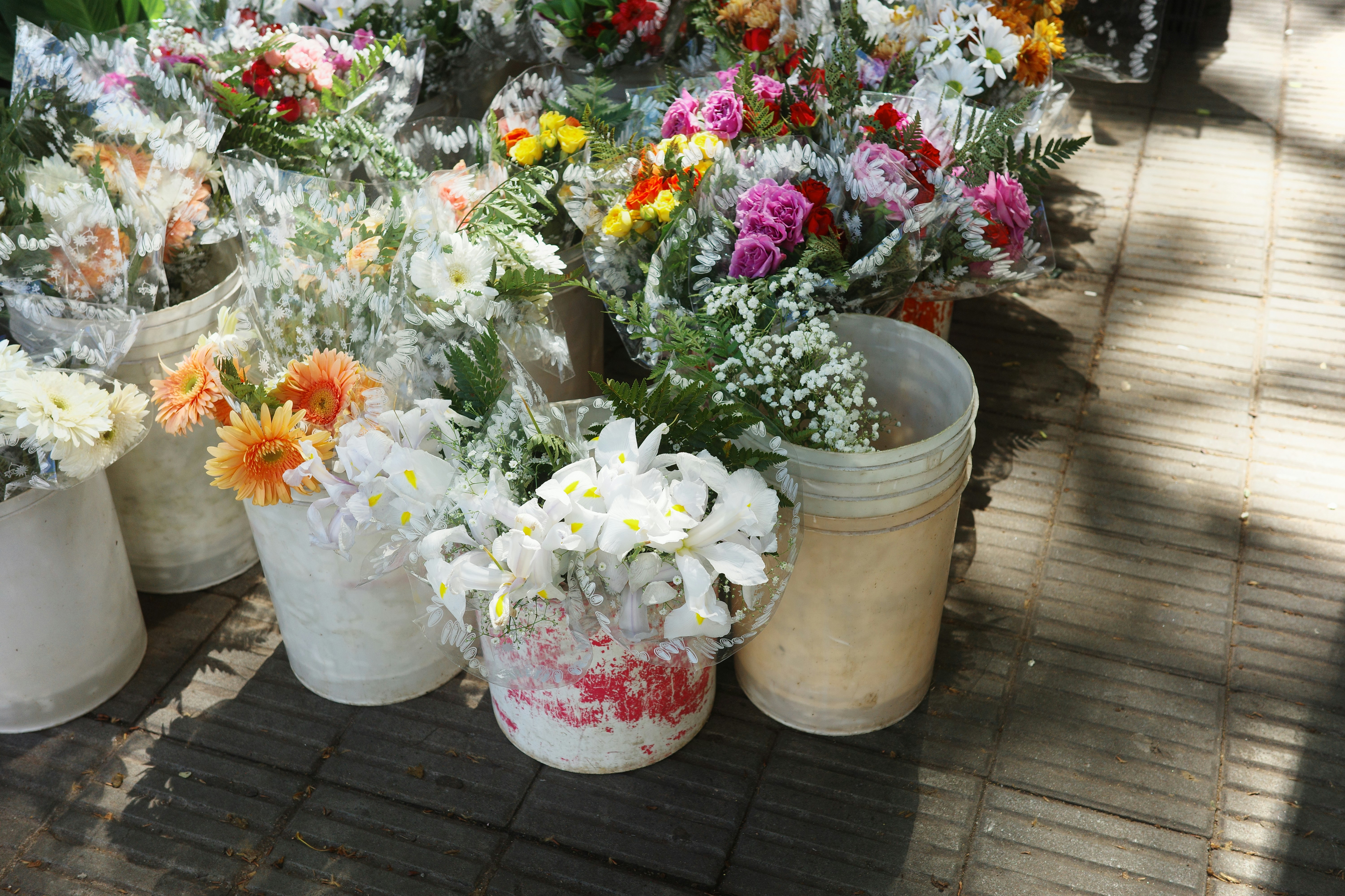 Buckets of colorful fresh flowers for sale on a paved sidewalk