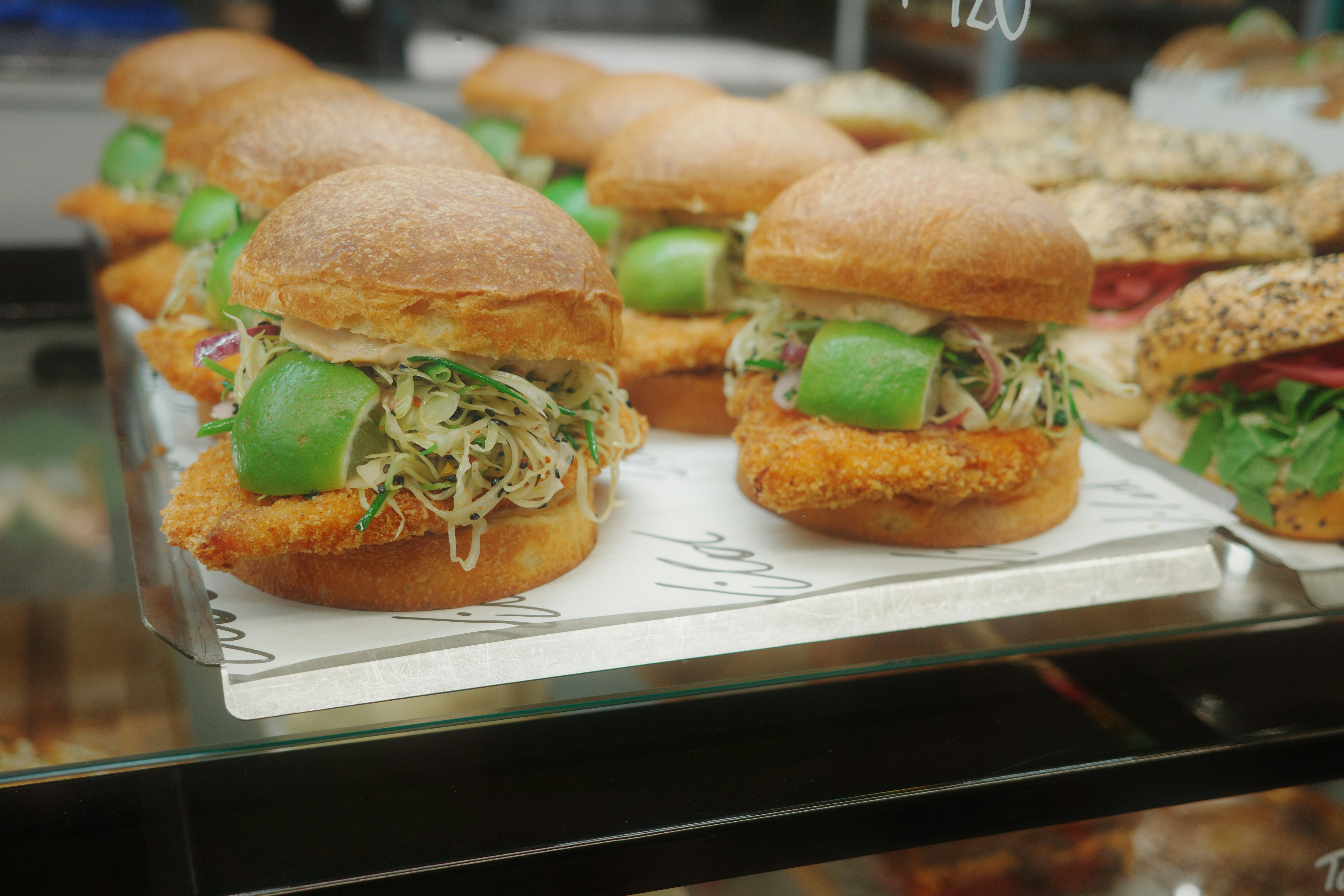 Crispy chicken sandwiches with lime wedges and shredded slaw on a display tray