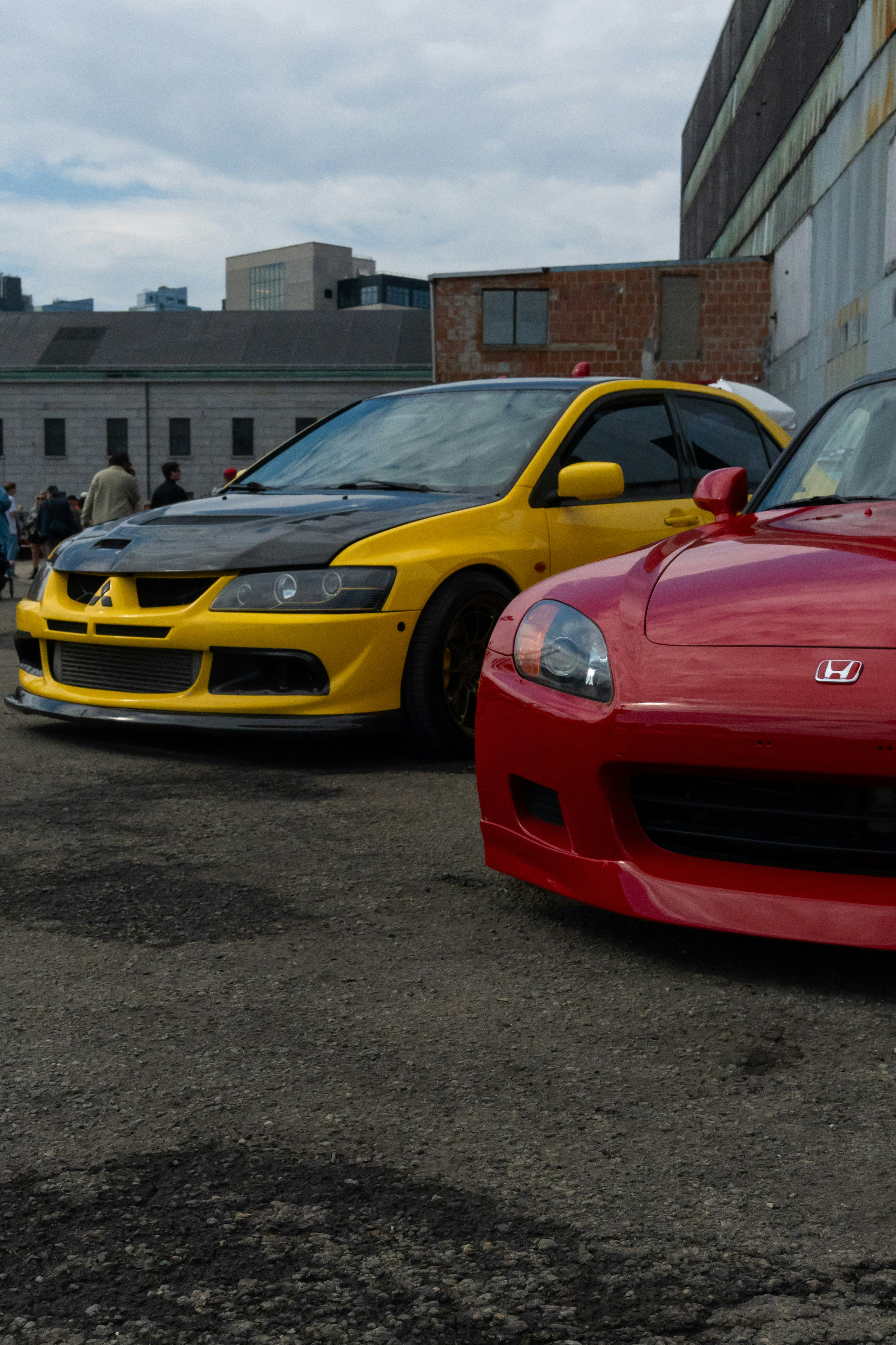 A yellow Mitsubishi Lancer Evolution and a red Honda S2000 parked on an asphalt lot
