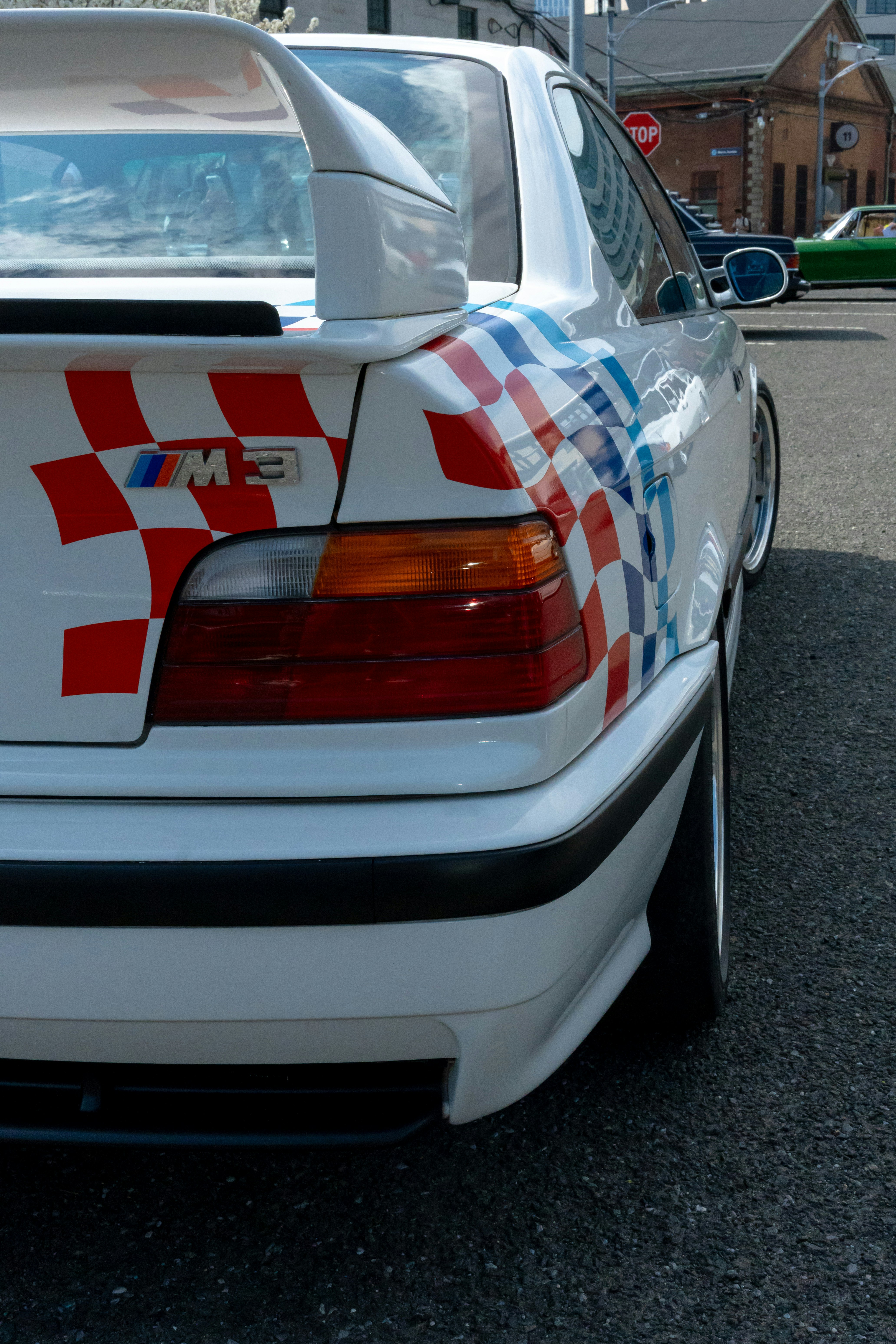 Das Heck eines weißen BMW M3 mit rot-blau karierten Rennaufklebern