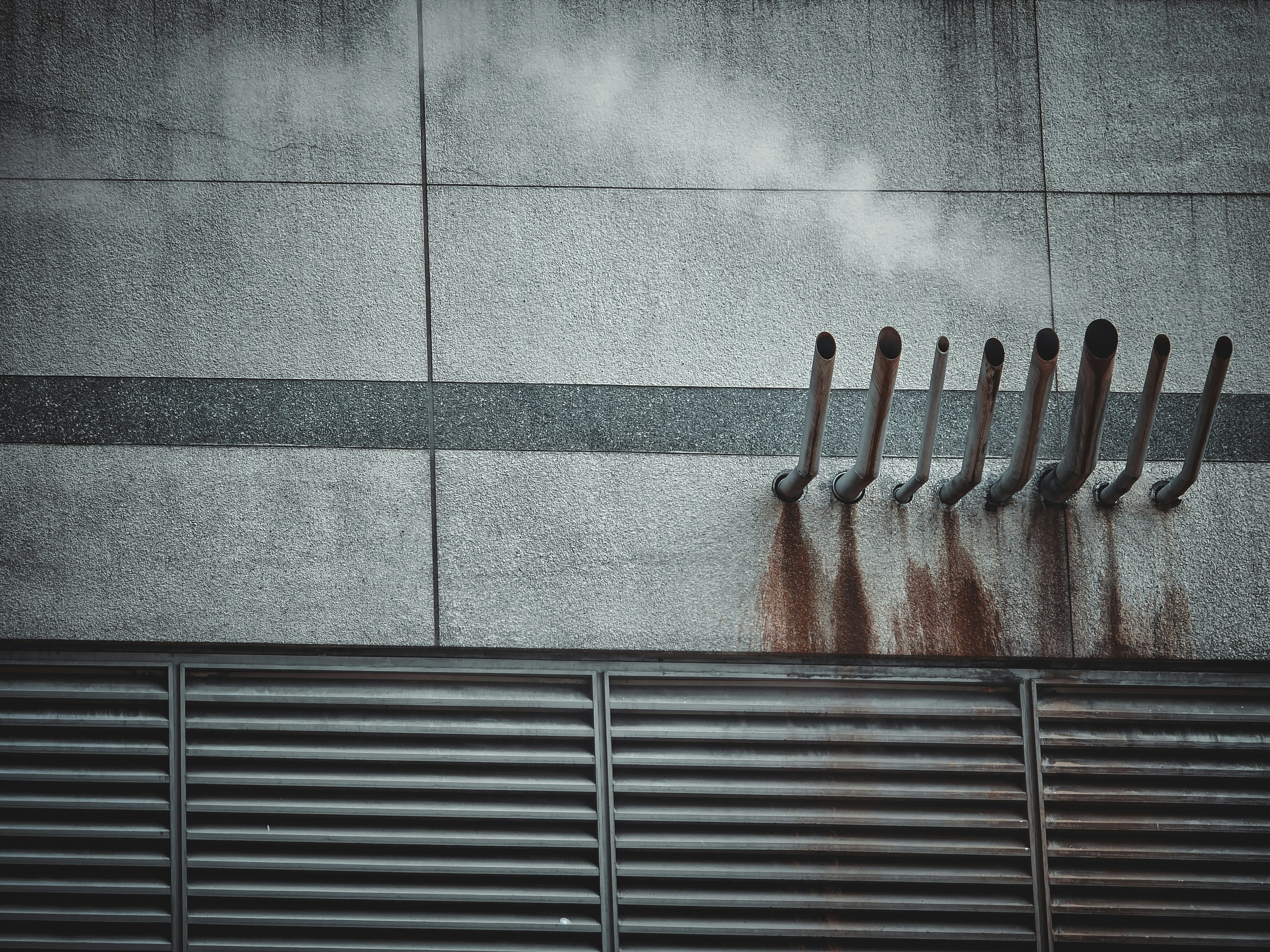 Steam rising from a row of metal exhaust pipes on a textured concrete wall