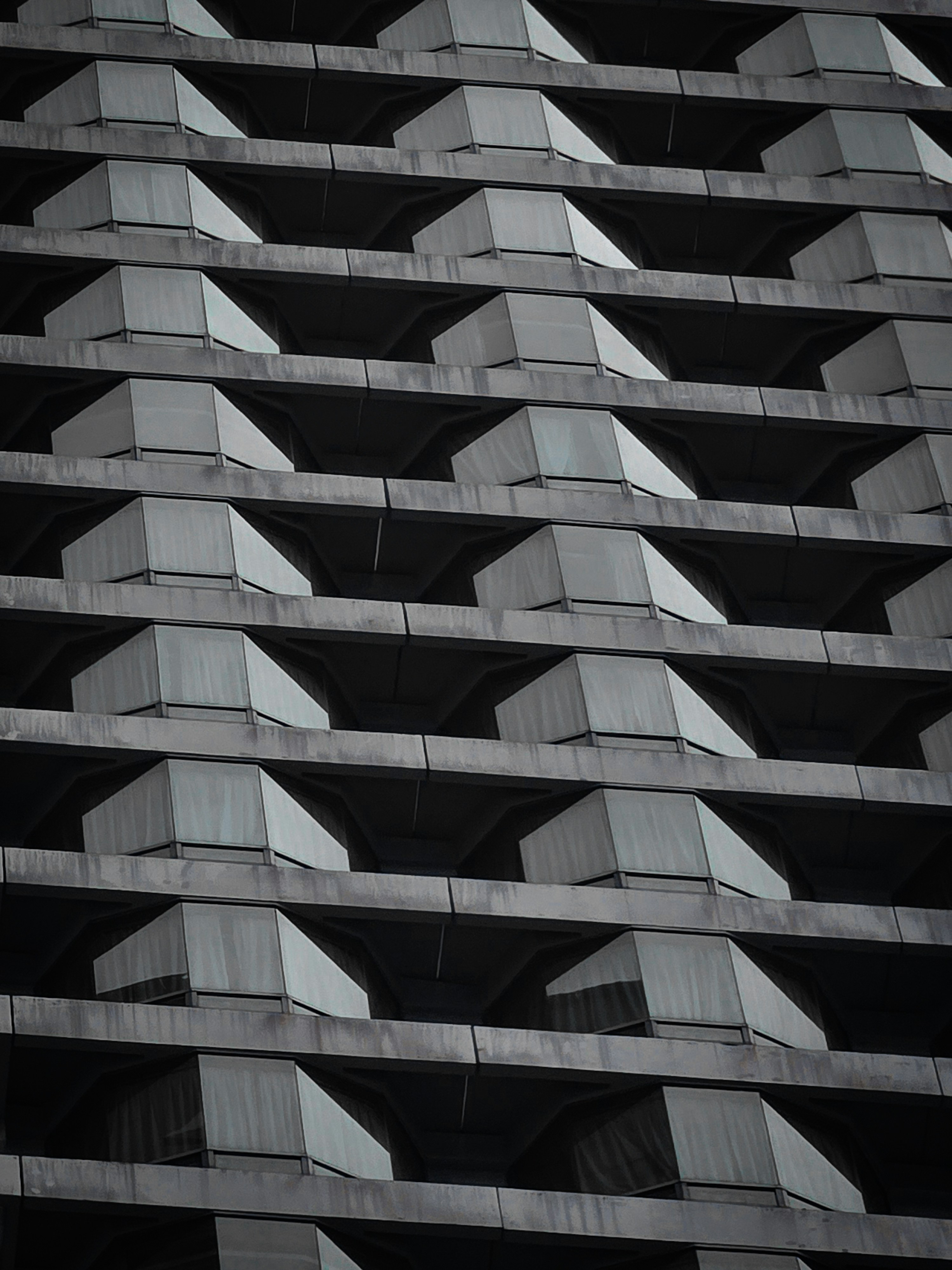 A repeating pattern of angular concrete balconies and glass windows on a modern building facade