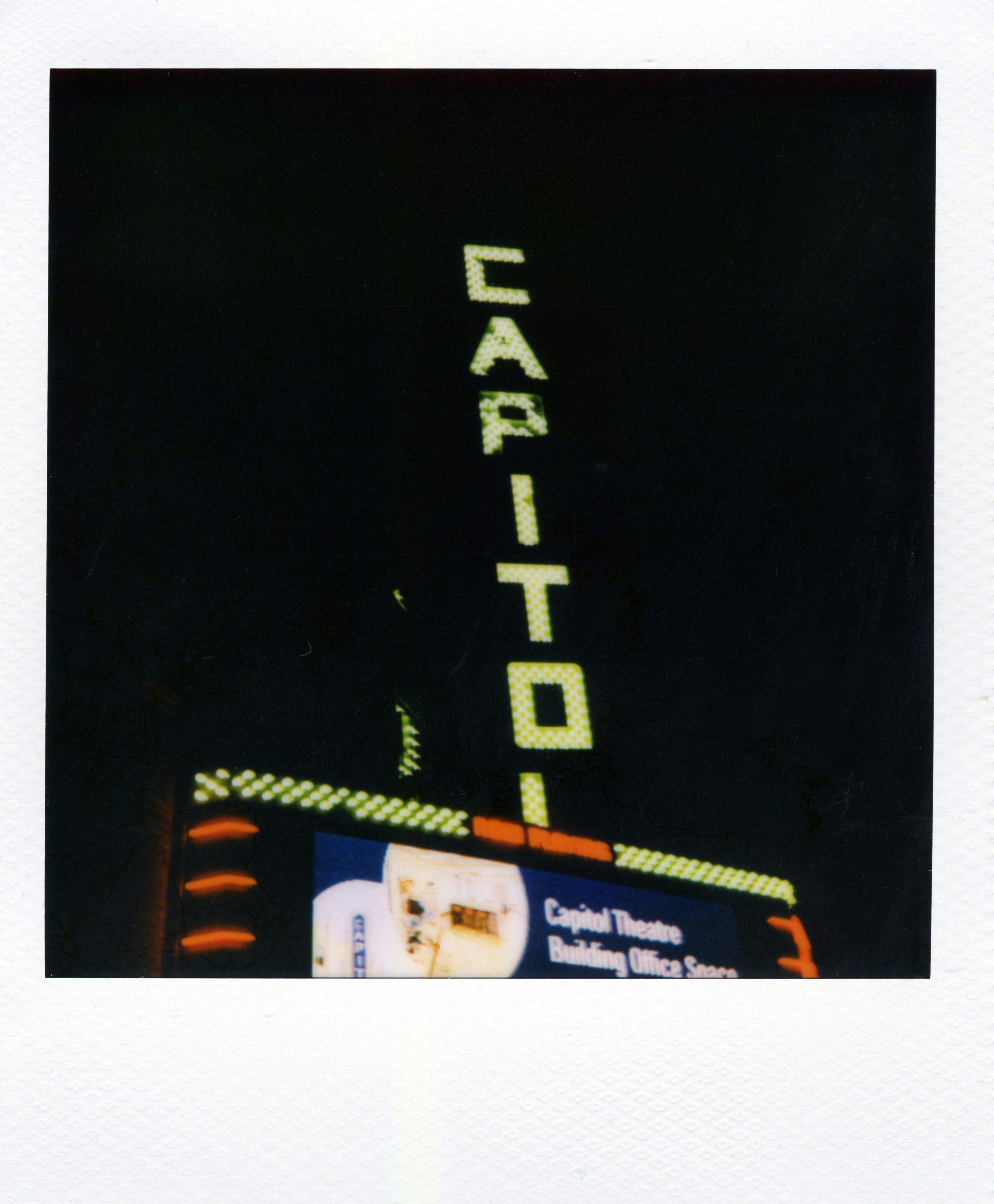 A vertical neon sign reading CAPITOL above a theatre building at night