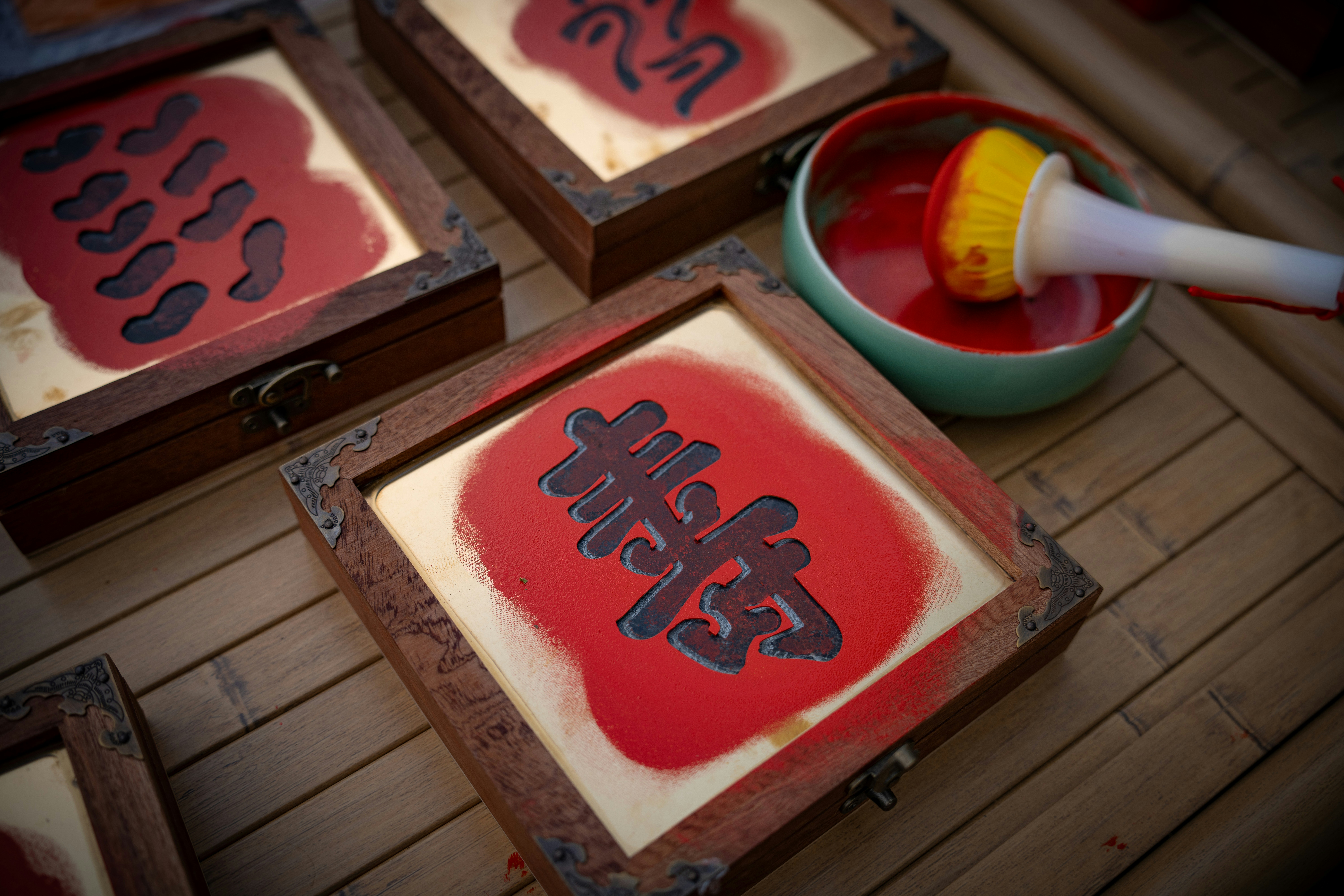 Wooden framed boards with red stenciled characters beside a bowl of red ink on a bamboo mat