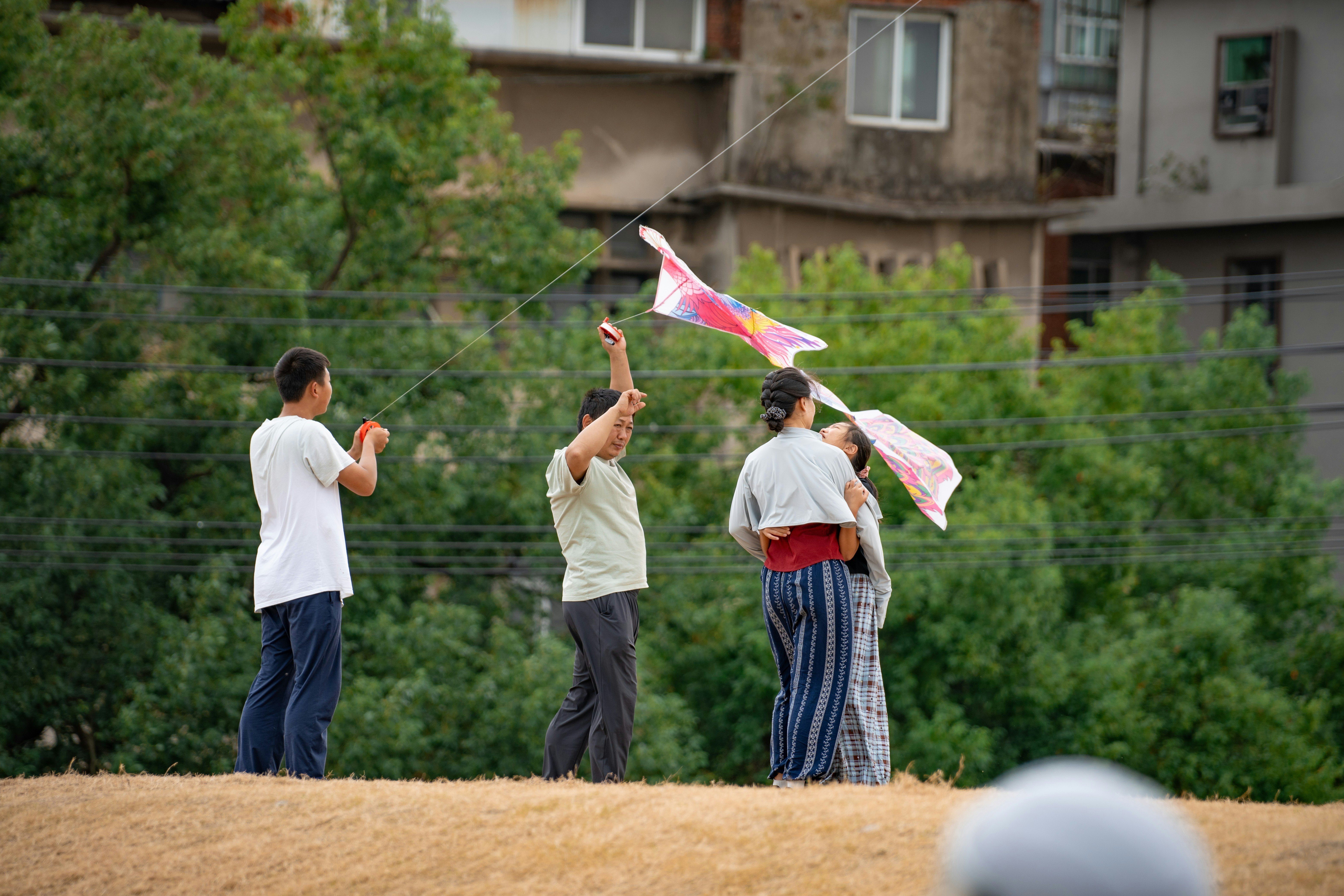 A family flying a colorful kite on a grassy hill with buildings in the background