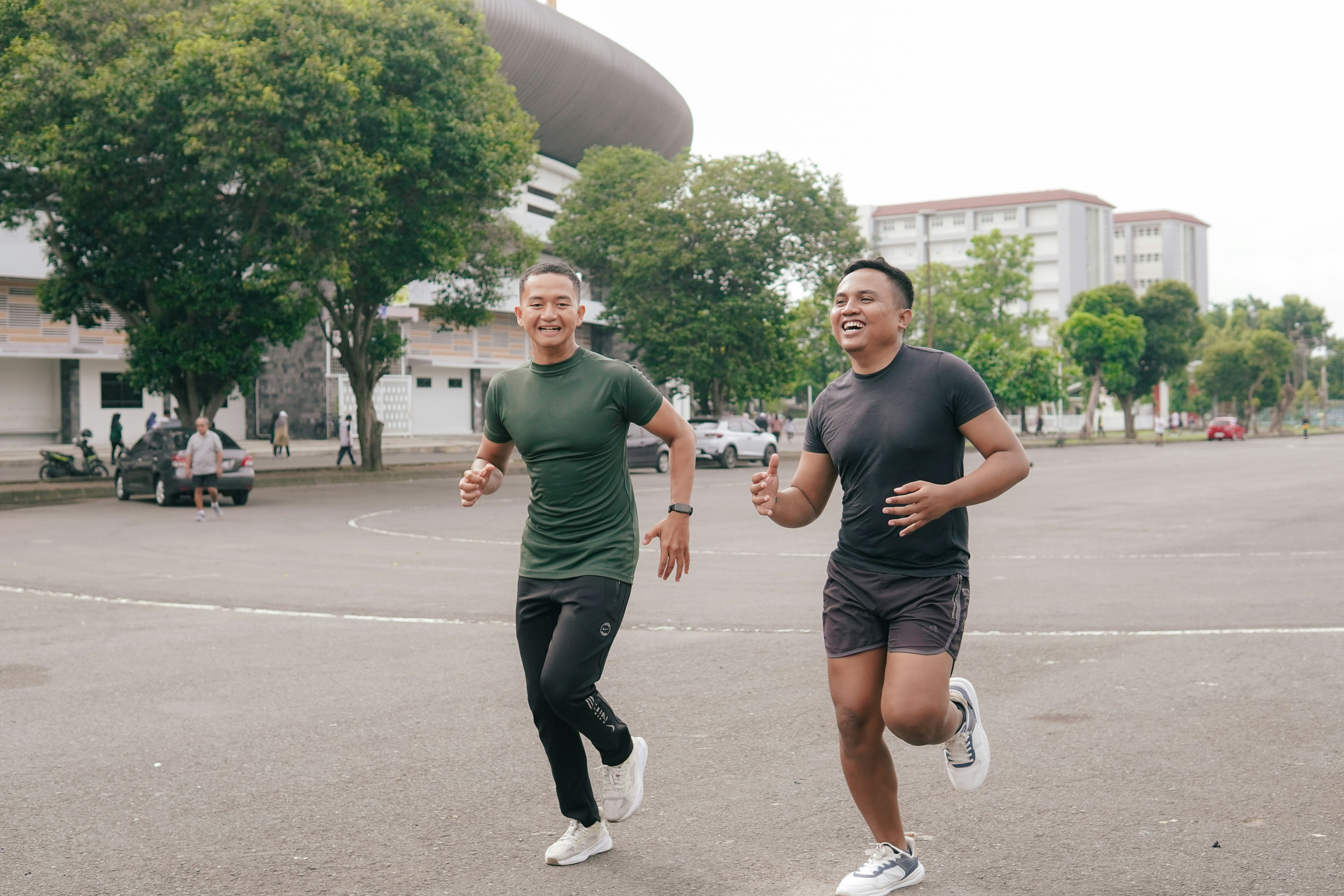 Two men jogging together on an asphalt lot near a large stadium