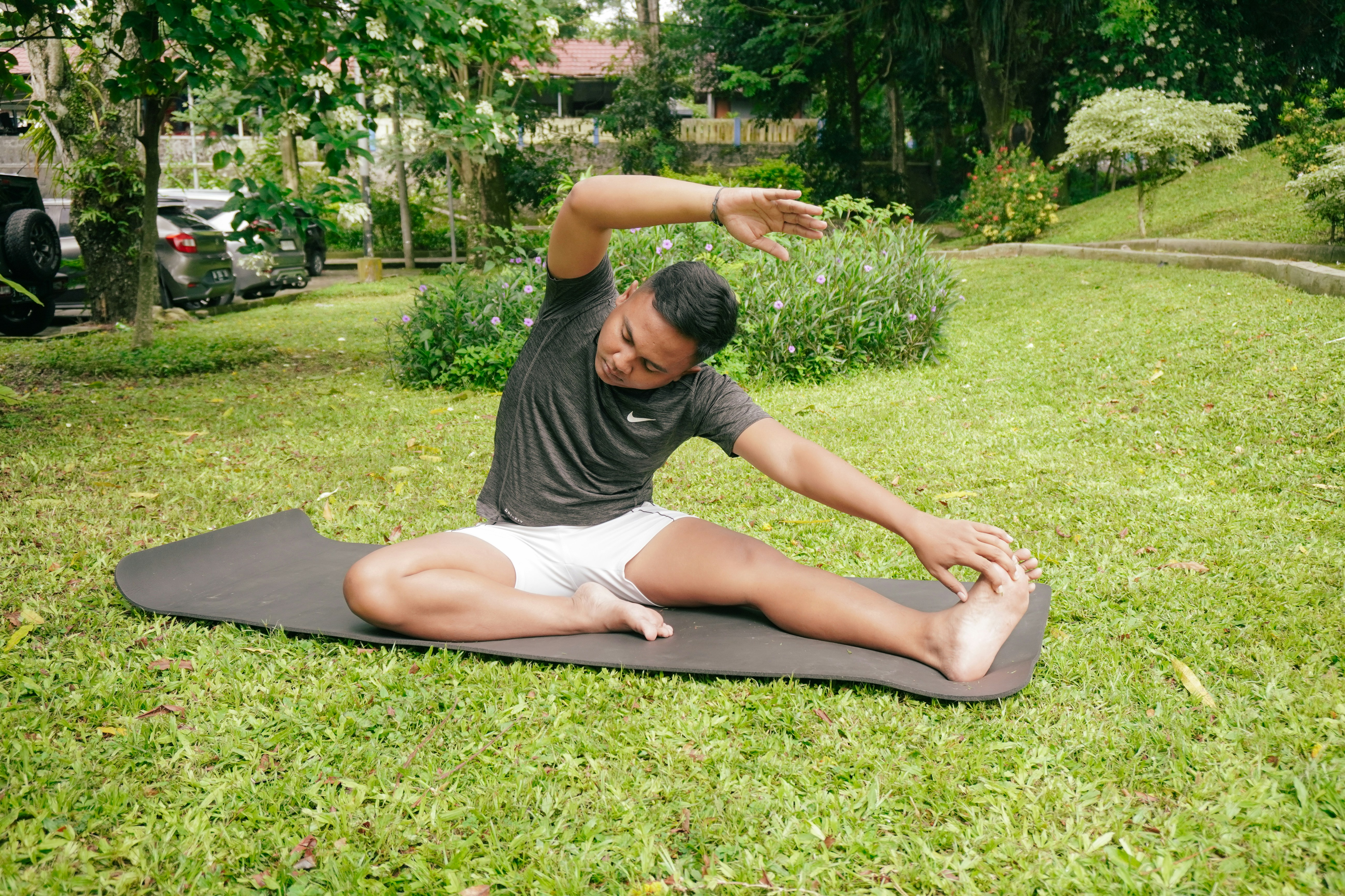 A man in a grey t-shirt and white shorts stretching on a black yoga mat outdoors
