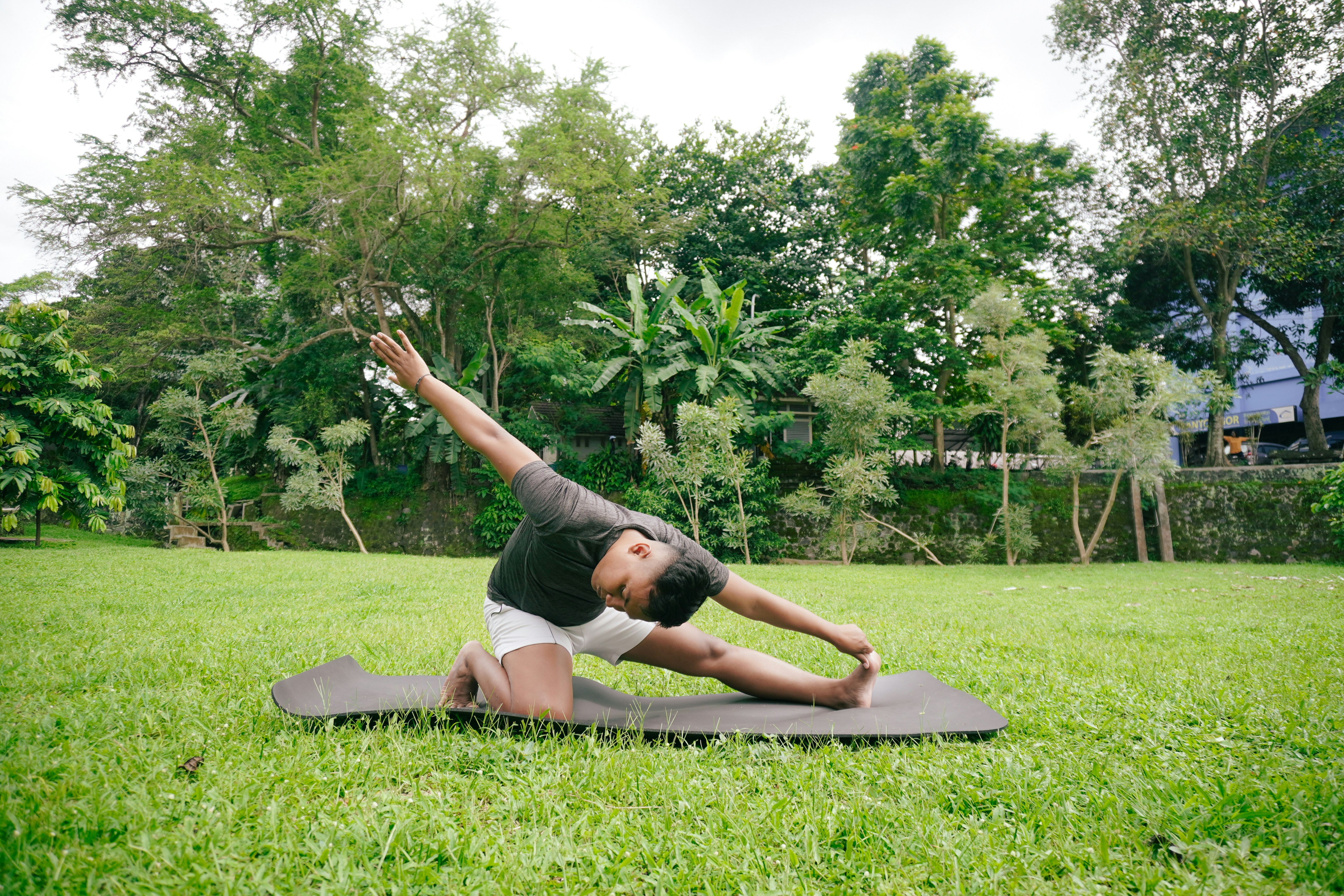 A man stretching on a yoga mat in a green park