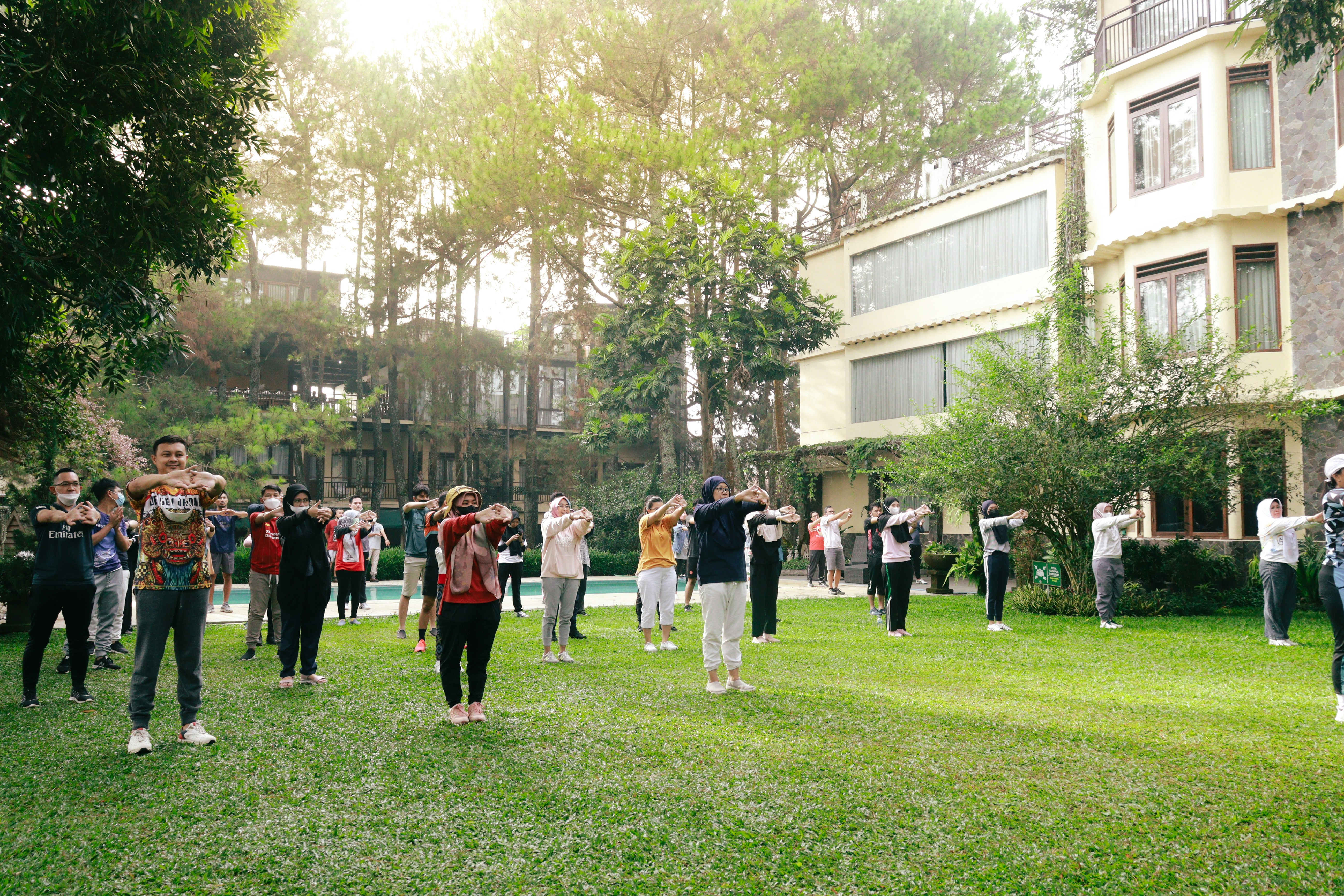 A group of adults exercising on a green lawn in front of a hotel