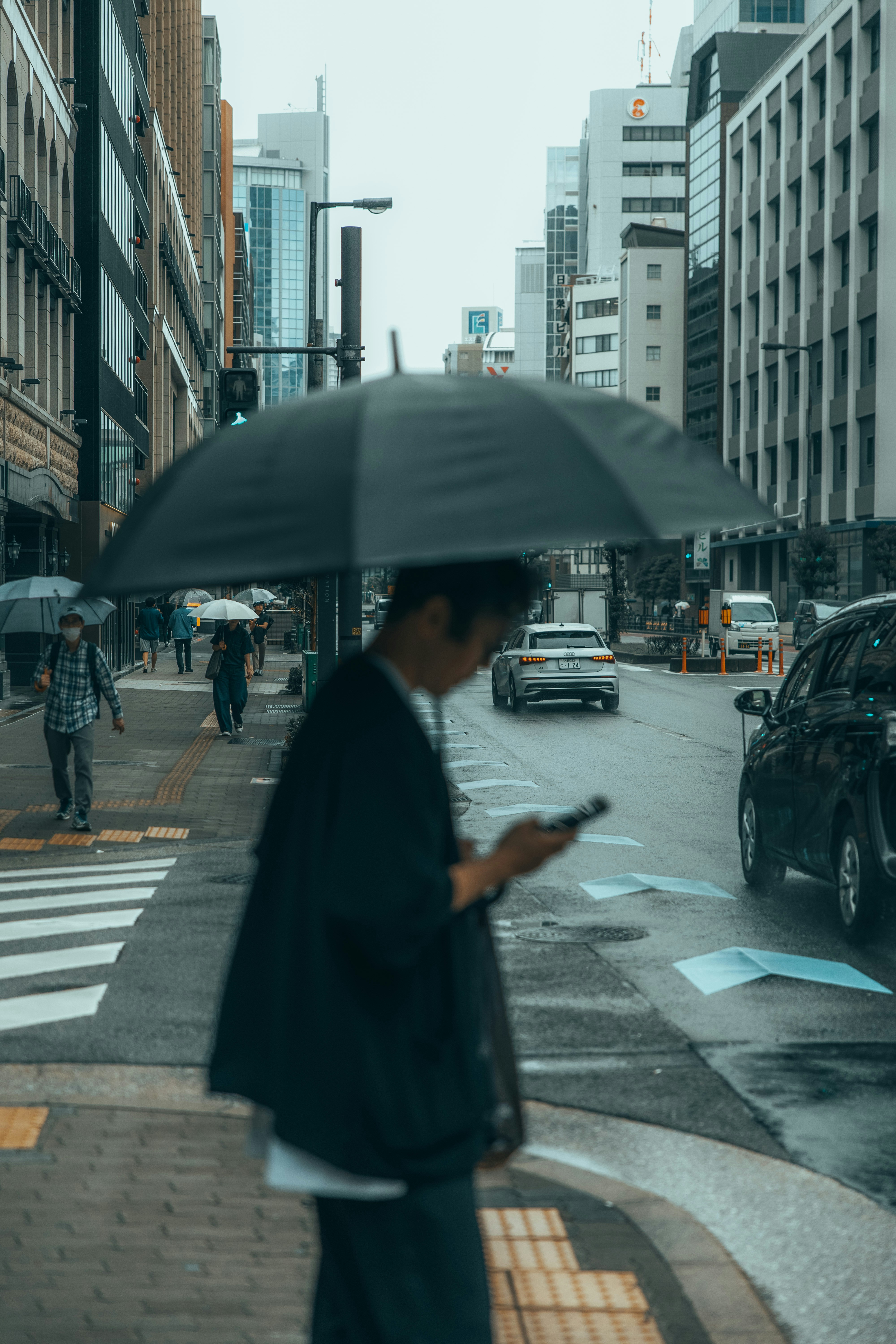 Una persona sosteniendo un paraguas y un teléfono en una calle lluviosa de la ciudad de Japón