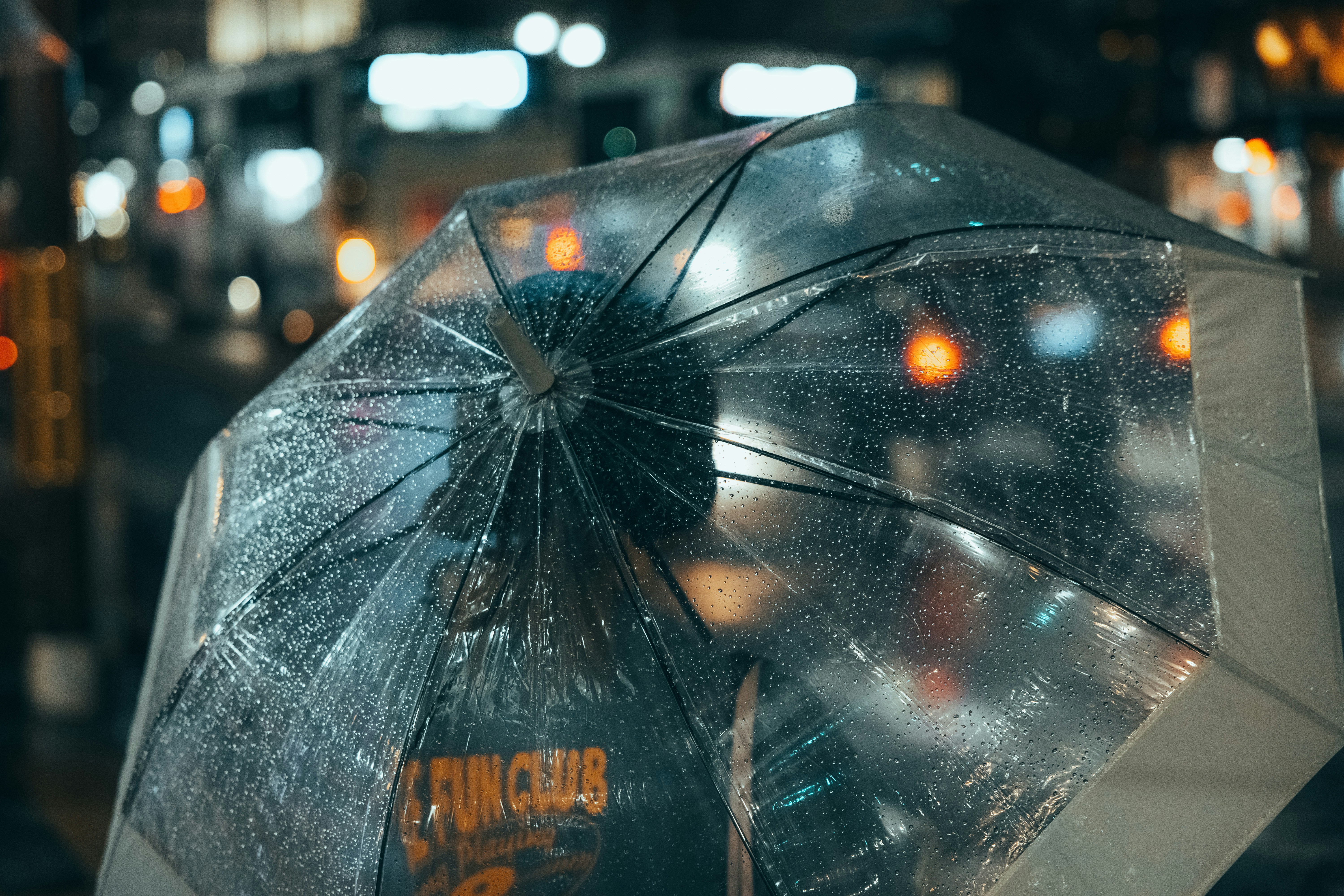 Una persona sosteniendo un paraguas transparente cubierto de gotas de lluvia en una calle de la ciudad por la noche