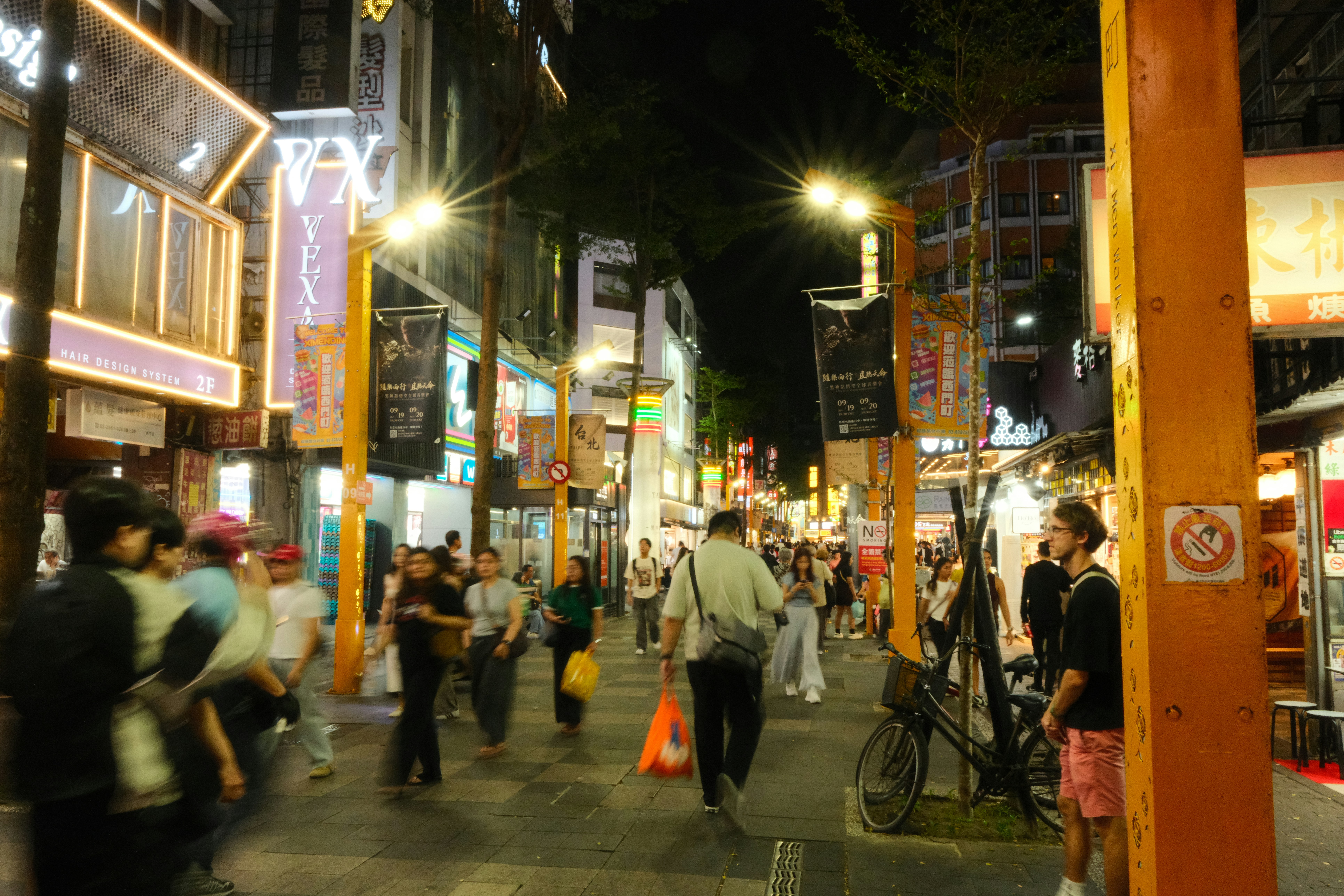 People walking along a busy pedestrian street in Taipei at night with bright neon signs