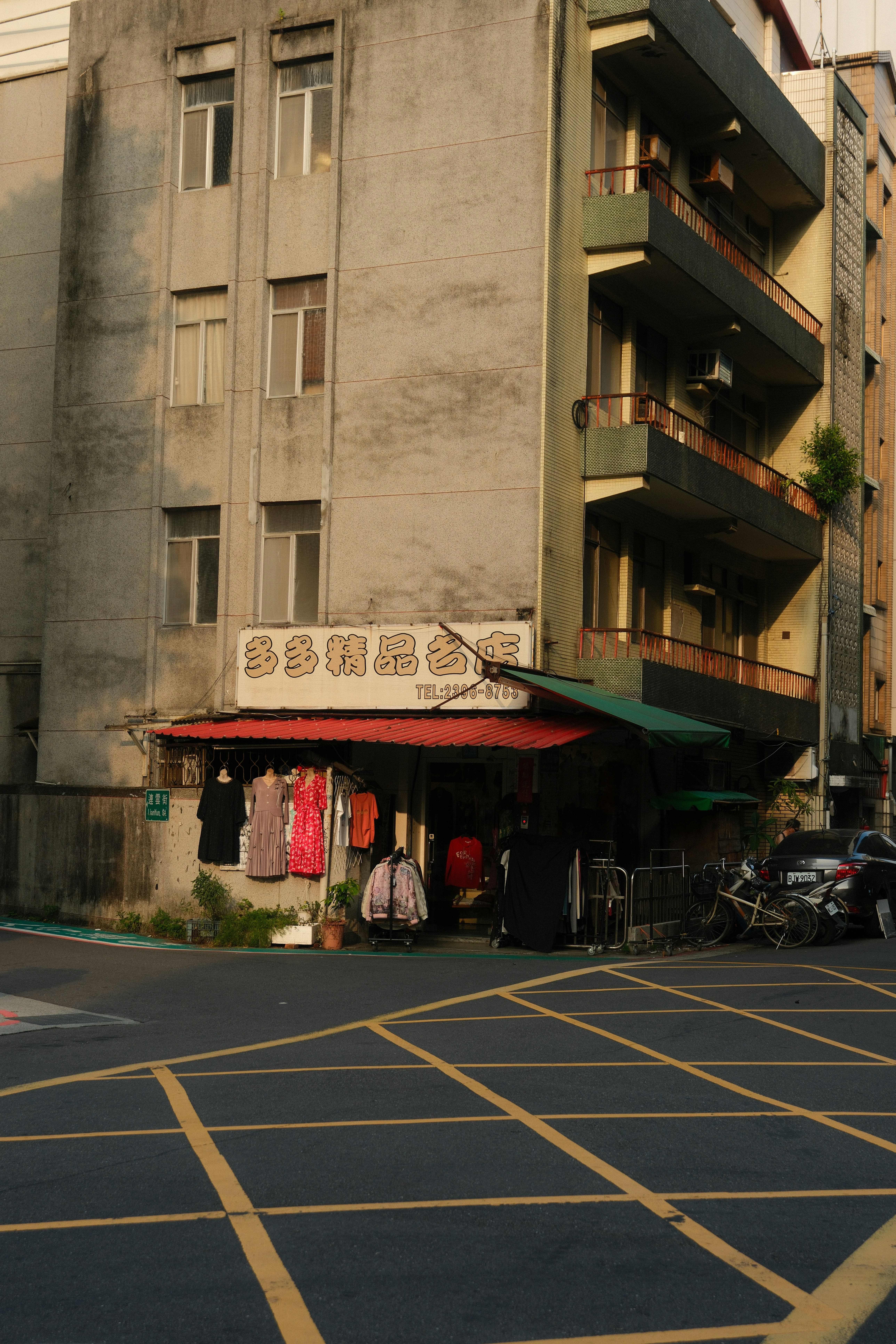 A small clothing shop on a street corner with garments hanging under a red awning